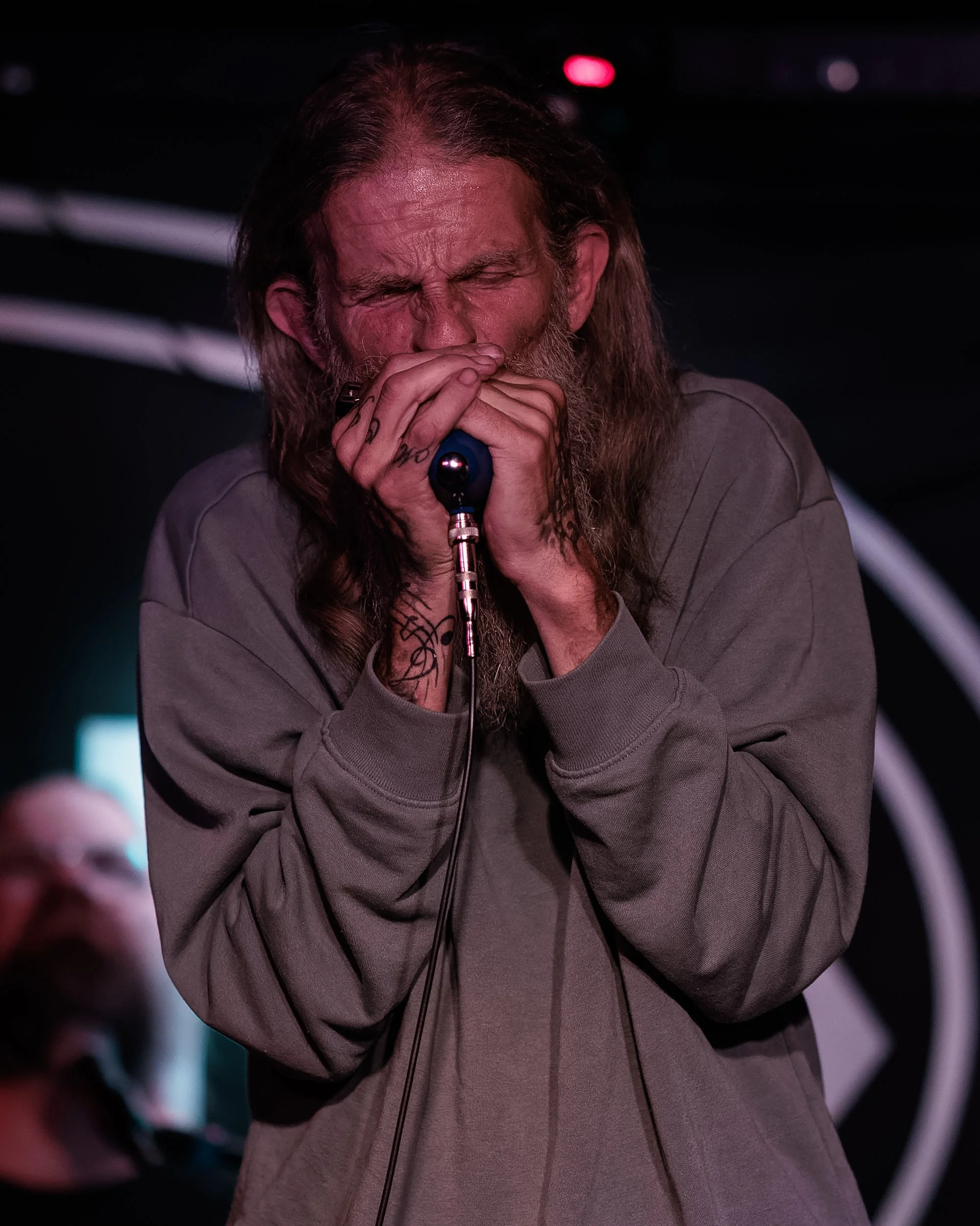 A man with long hair and a beard passionately singing into a microphone during a live performance, with his eyes closed and gripping the microphone tightly.