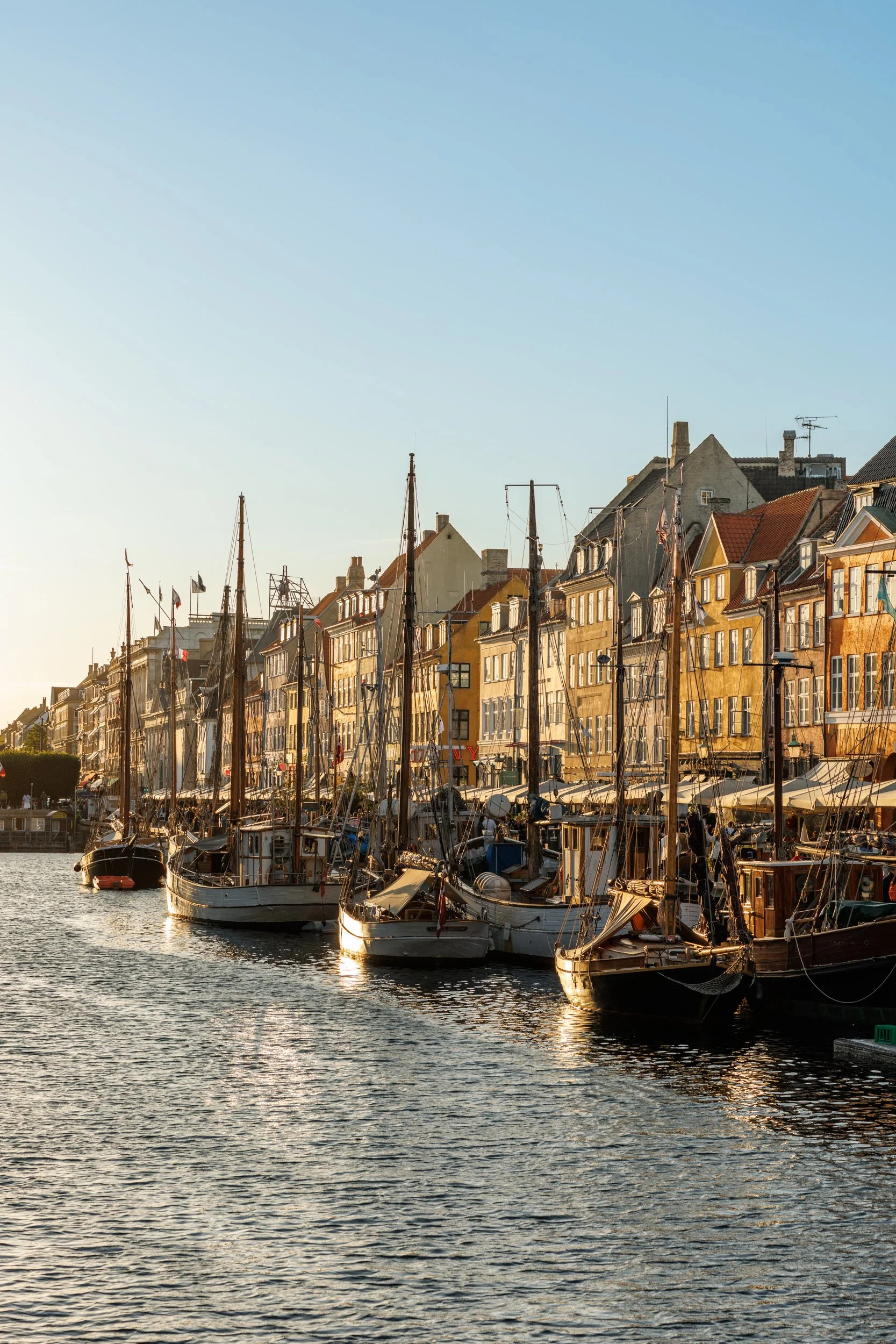 A harbor with sailboats docked, and colorful historic buildings with red and yellow facades along the waterfront, under a clear blue sky.