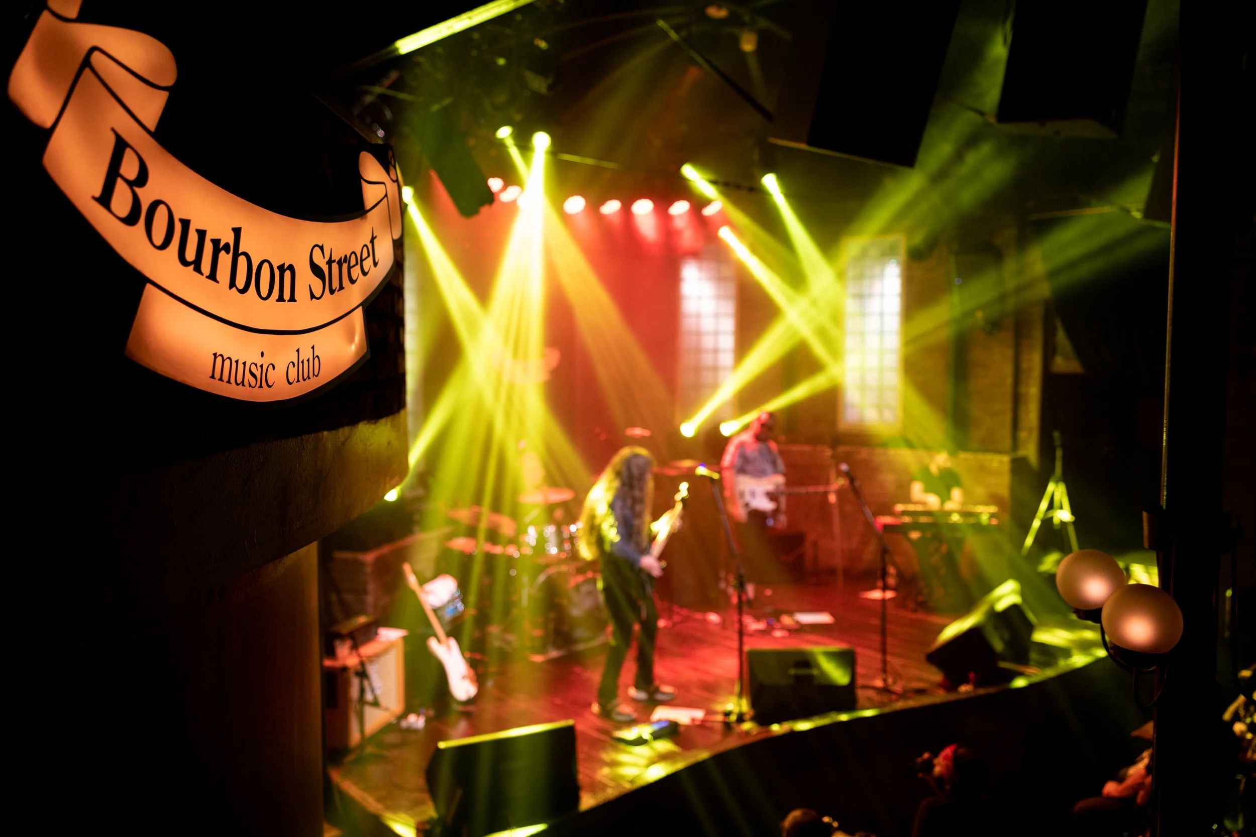 View of a live music performance at a jazz club with yellow and red stage lights and musicians playing instruments.