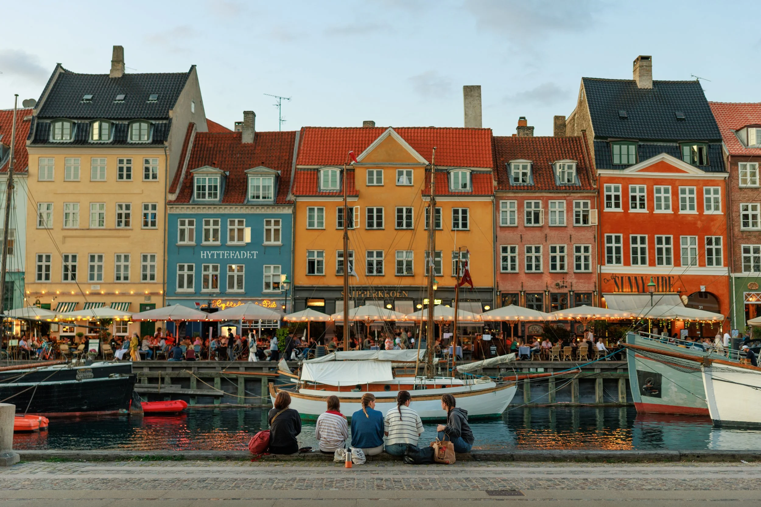 Colorful buildings on a waterfront with boats and people sitting and socializing near the water.