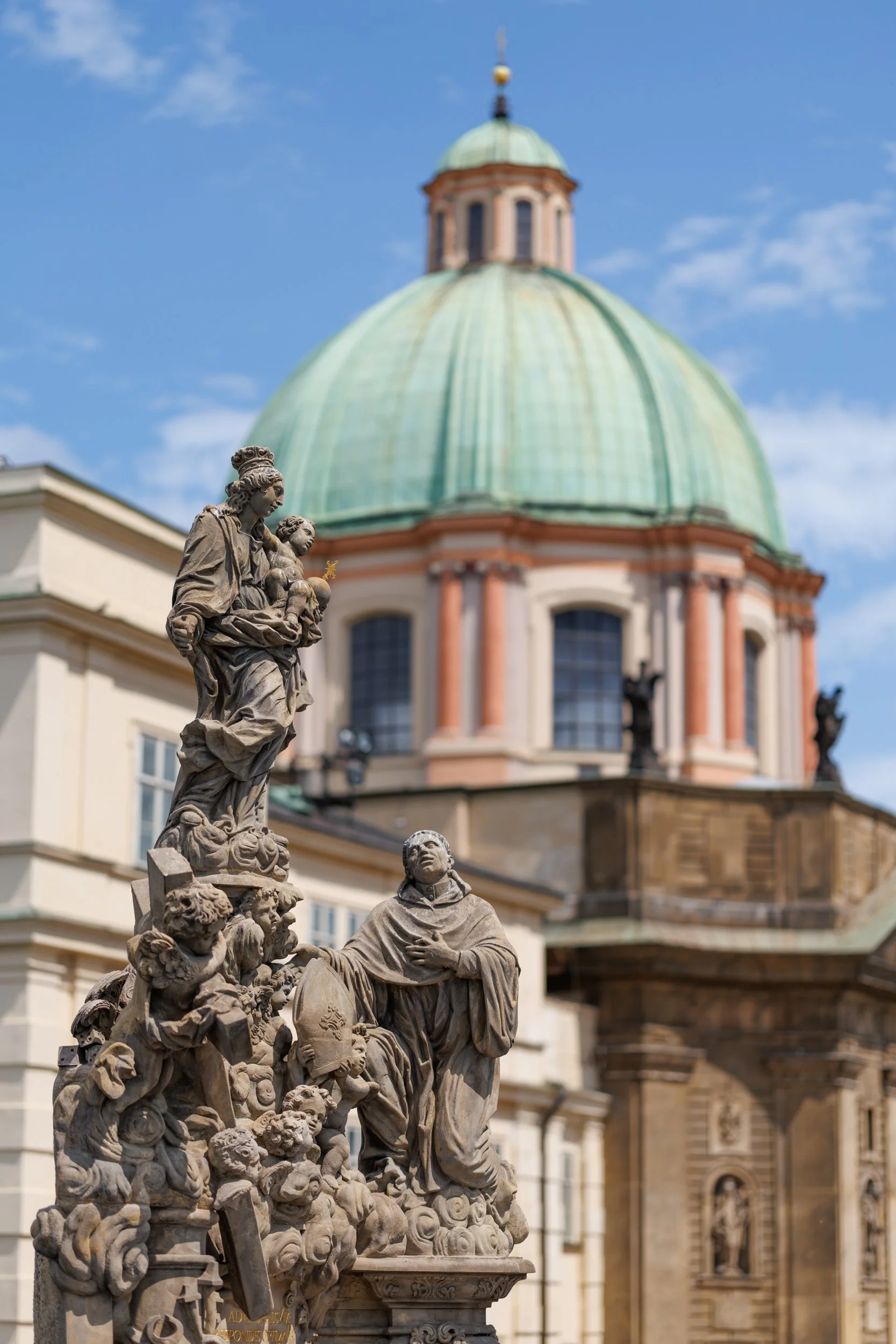 Close-up of a detailed stone sculpture depicting a group of figures, with a domed building in the background under a partly cloudy sky.