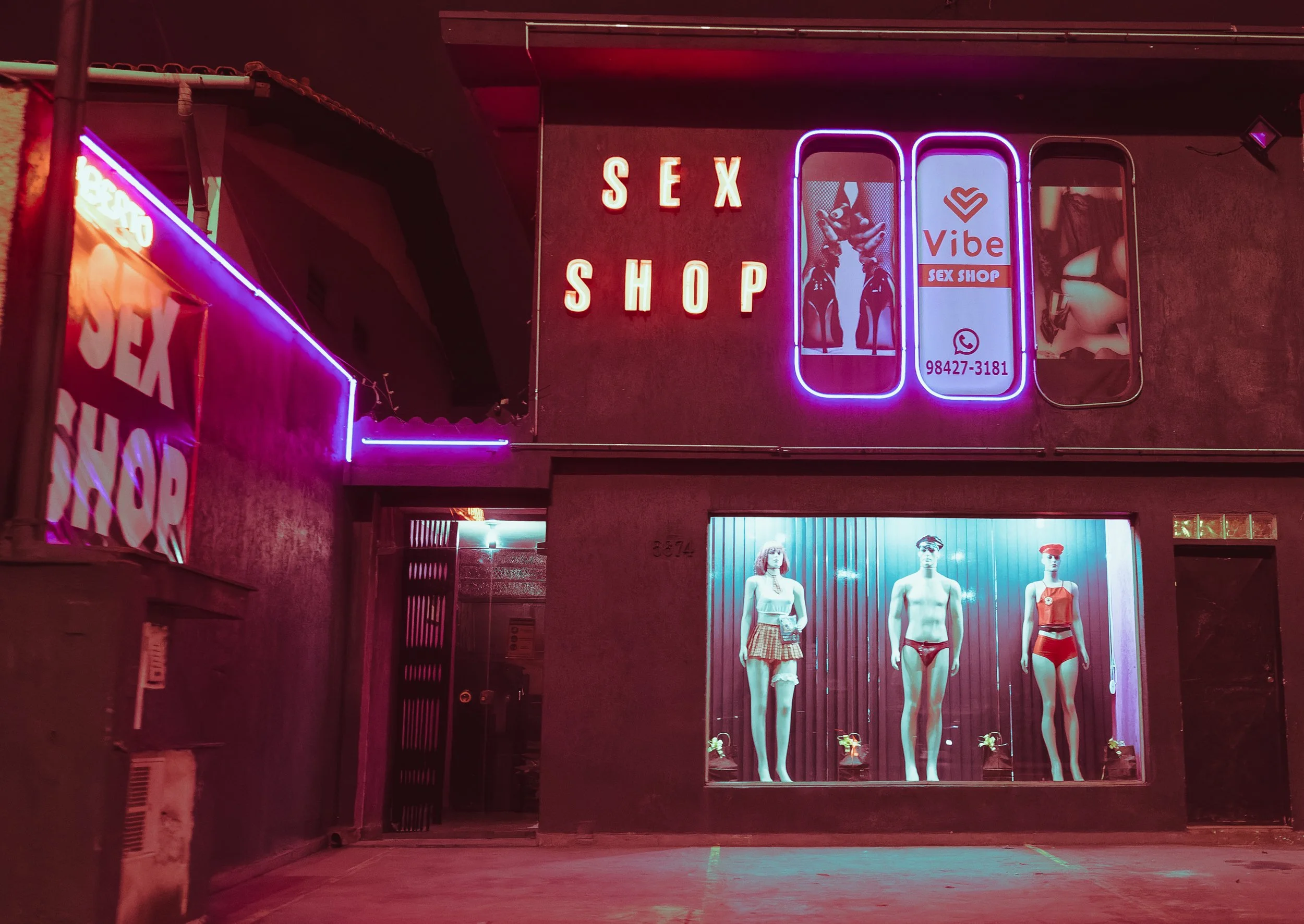 Neon signage of an adult shop with mannequins in underwear displayed in the window.