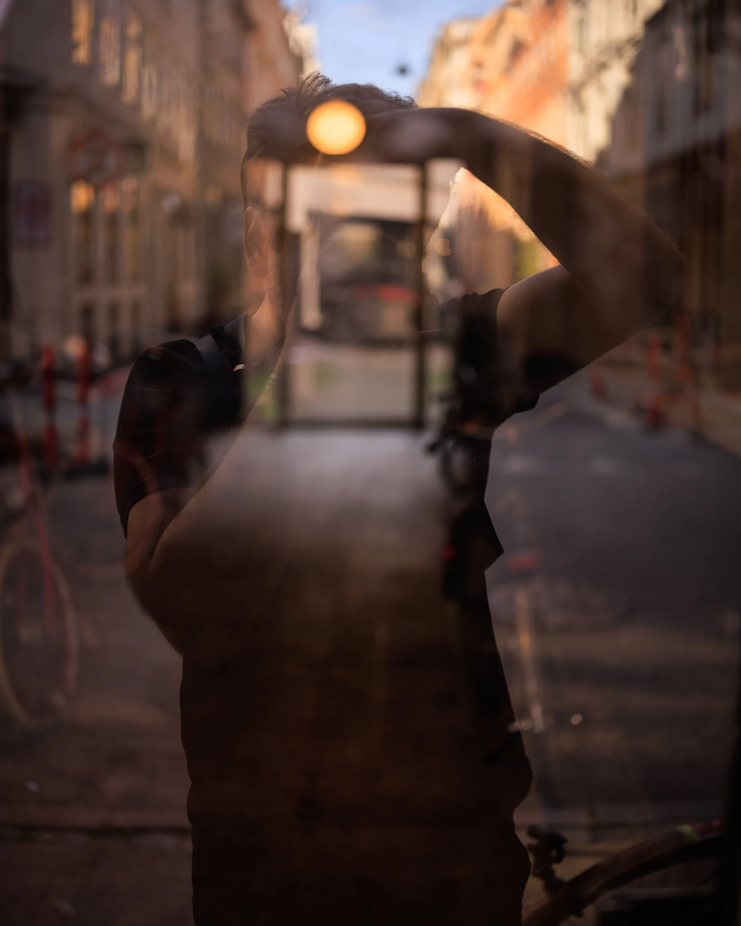 Reflection of a person taking a photo with a smartphone in a glass window of a city street during sunset.
