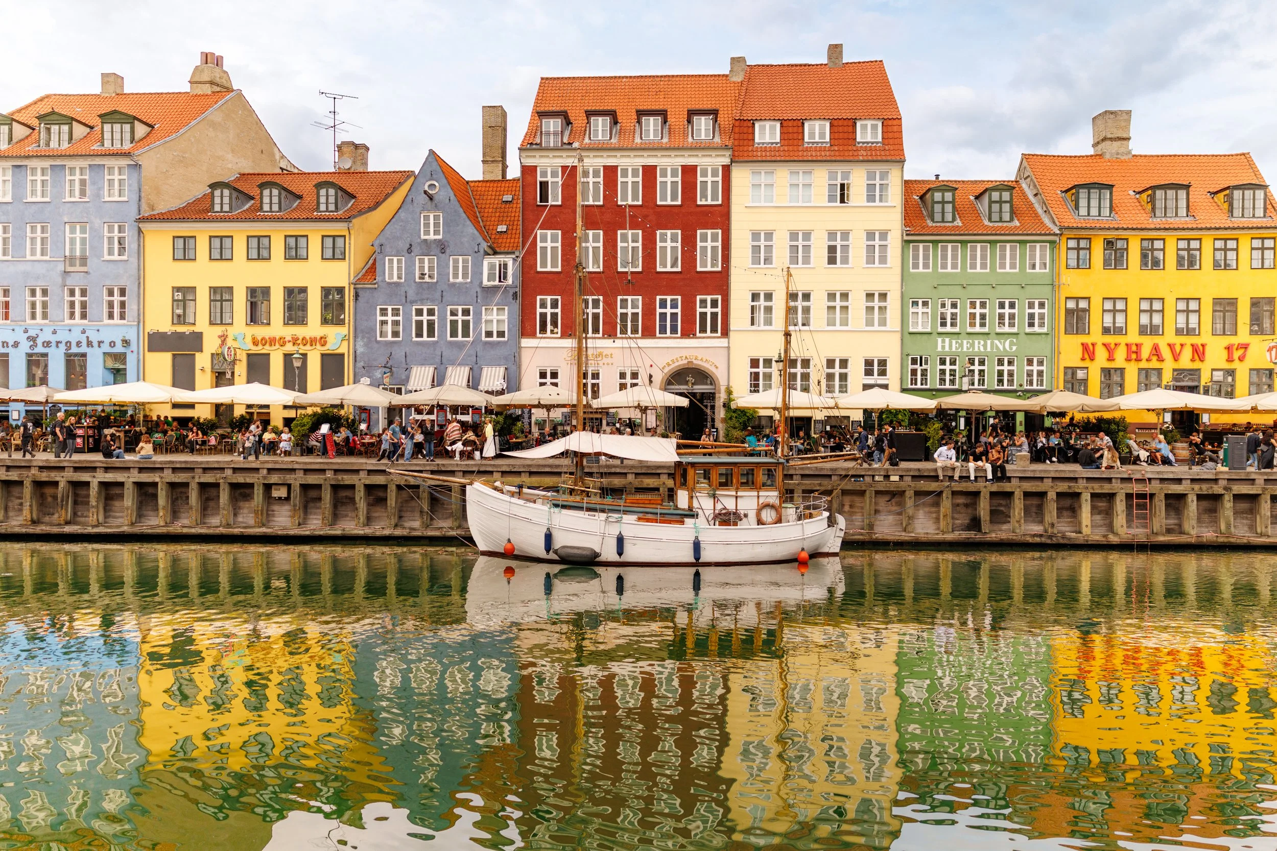 Colorful buildings along a waterfront with outdoor seating, boats, and reflections in the water.