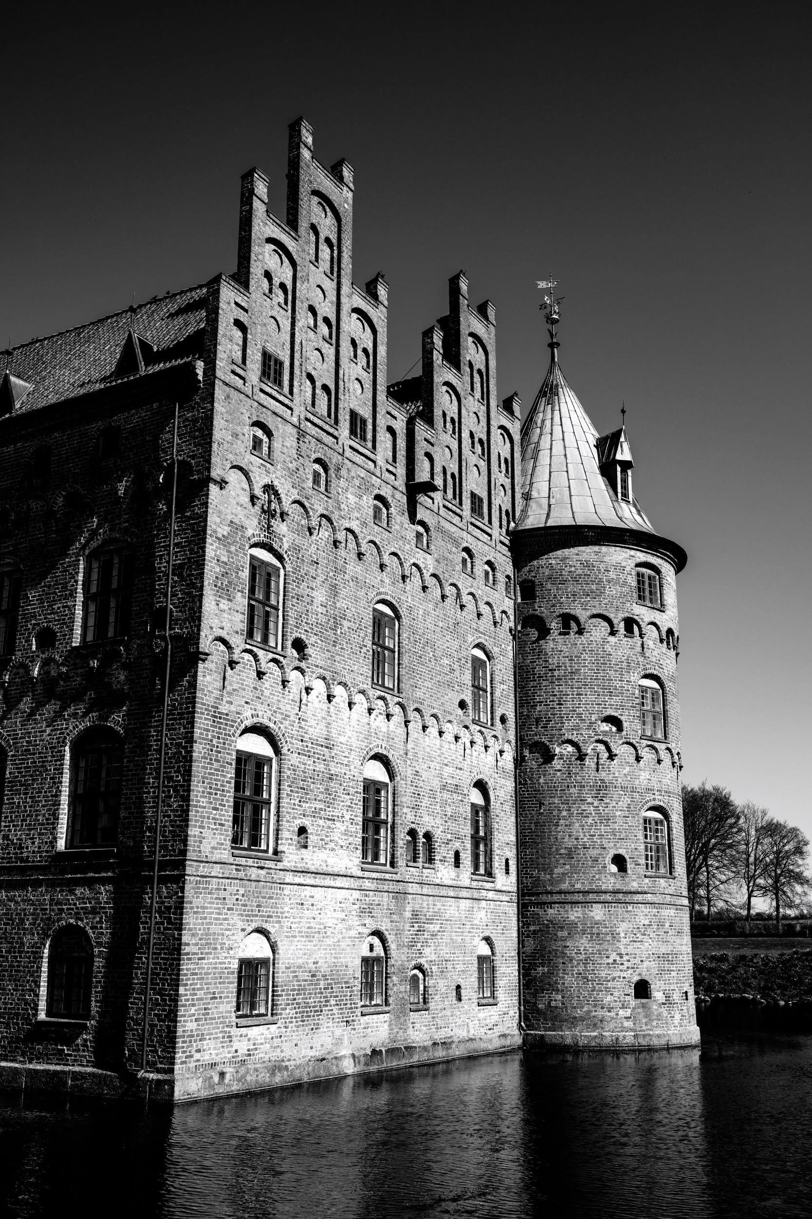 Black and white photo of a large medieval castle with multiple towers, surrounded by water, with dark skies in the background.