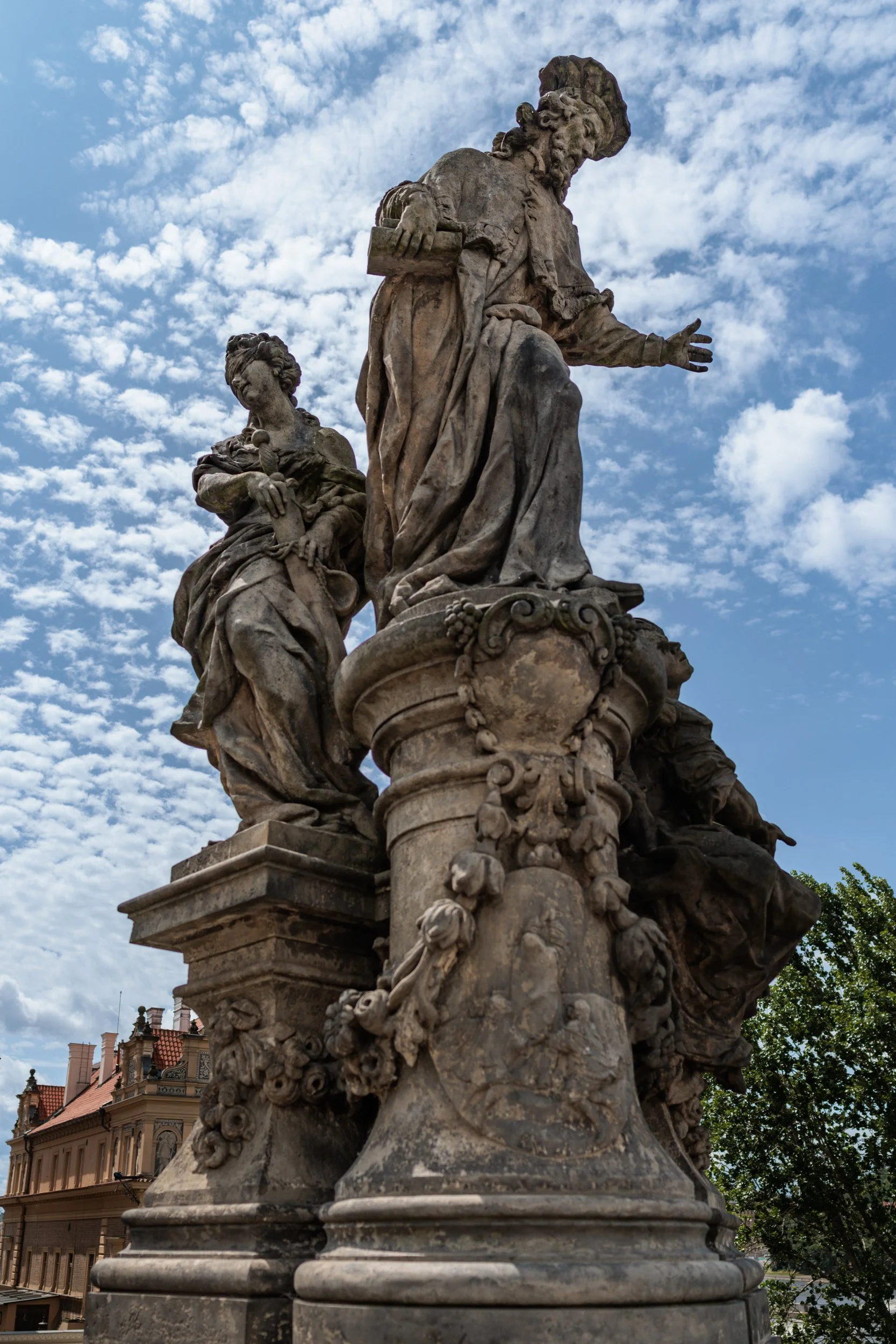 Close-up of an ornate stone or concrete fountain or sculpture with intricate carvings and figures, set against a partly cloudy sky.