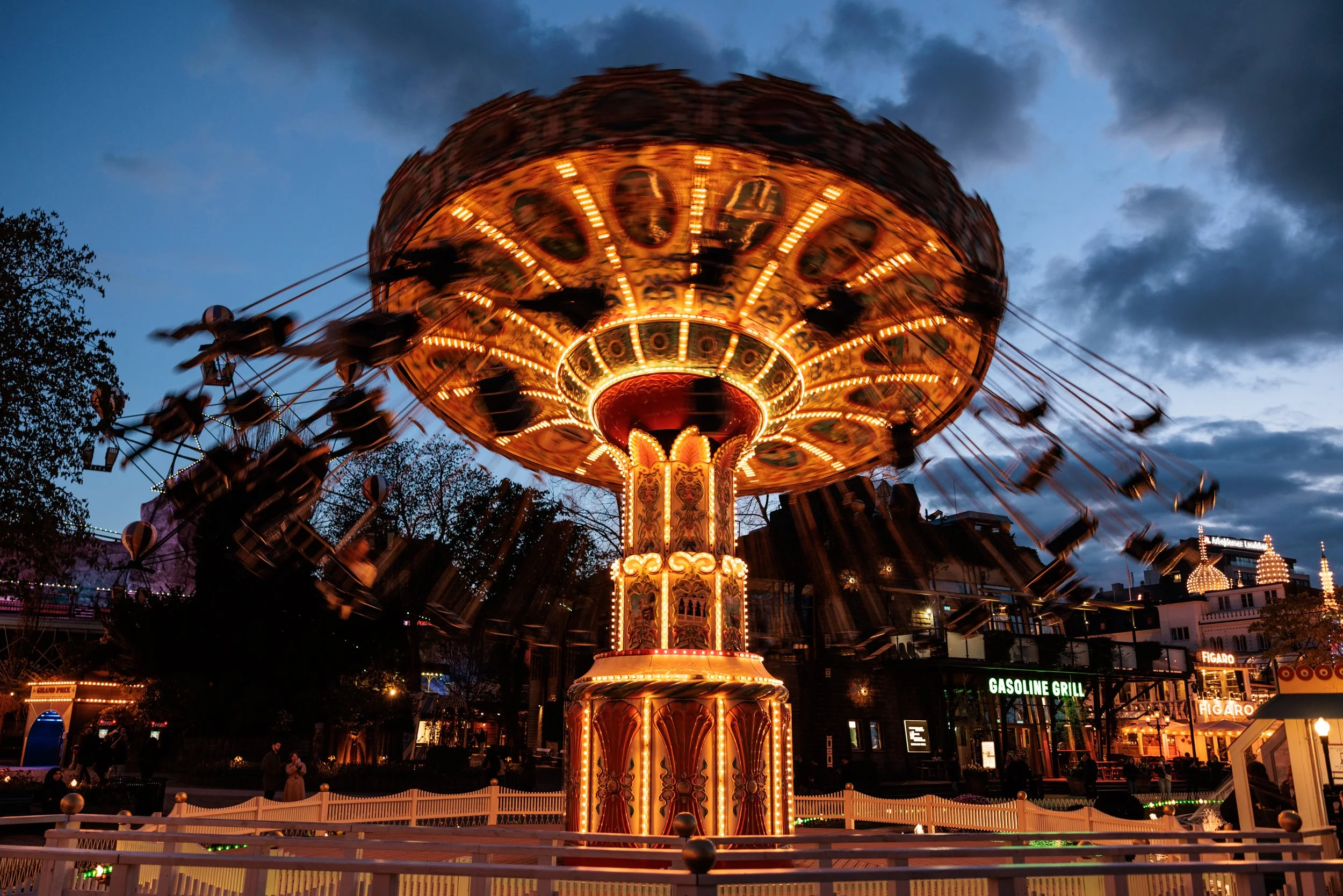 A brightly lit carousel swings ride at dusk with the sky darkening and clouds overhead.