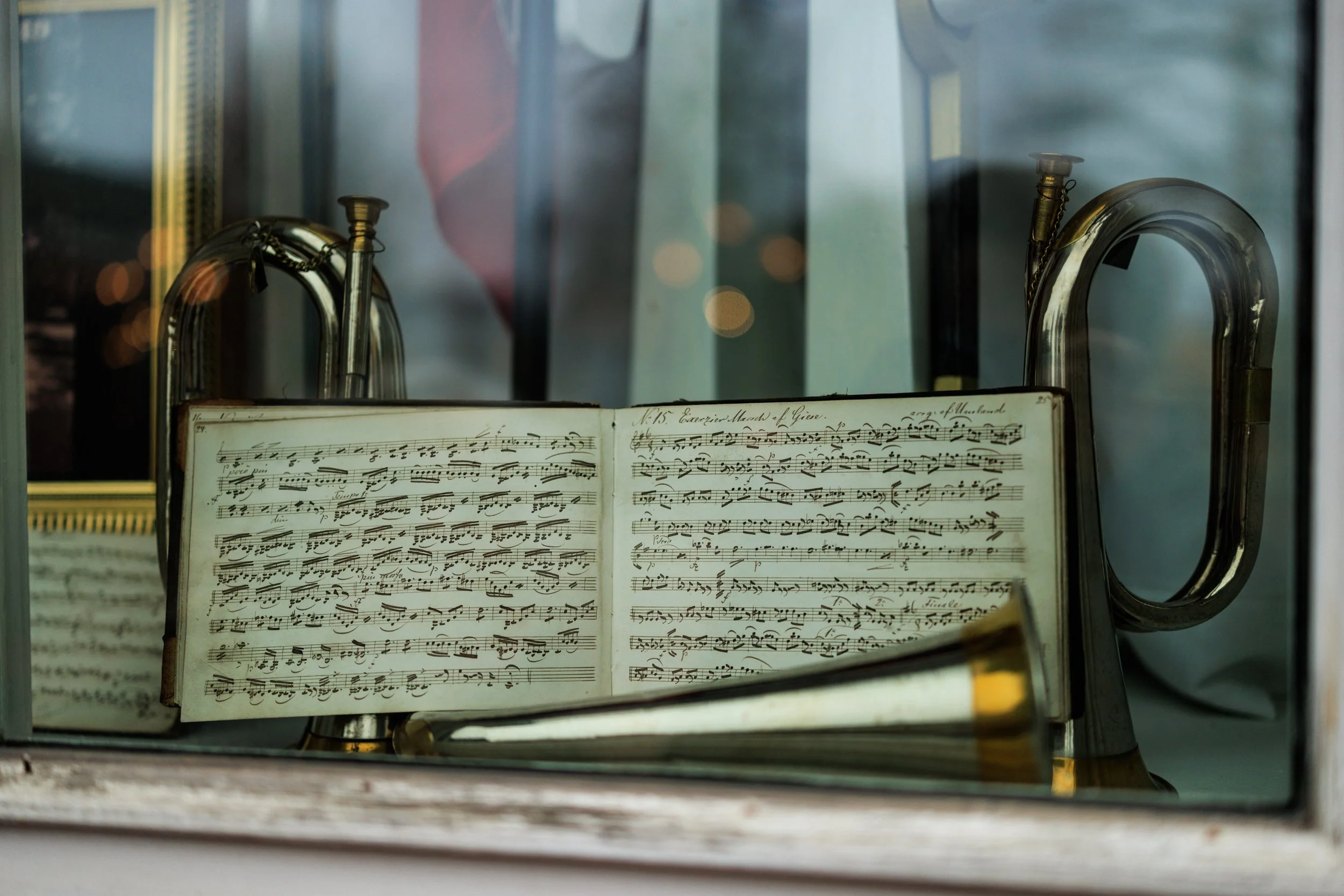 An open sheet music book displaying classical music notes and handwritten annotations, behind a glass or plastic barrier with metallic handles, possibly in a museum or display setting.