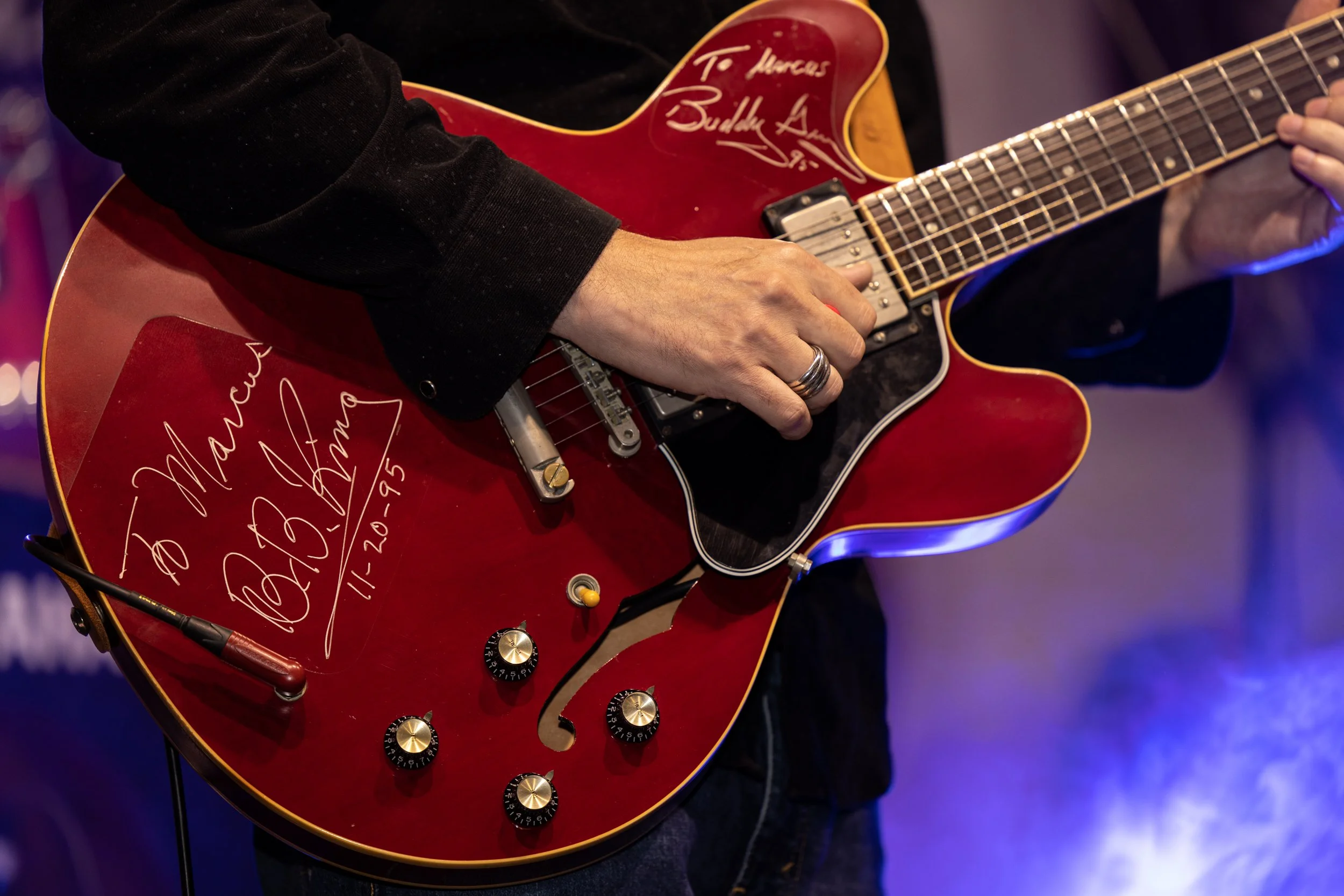 A person playing a red electric guitar with signatures and messages on it, wearing a black long sleeve shirt.