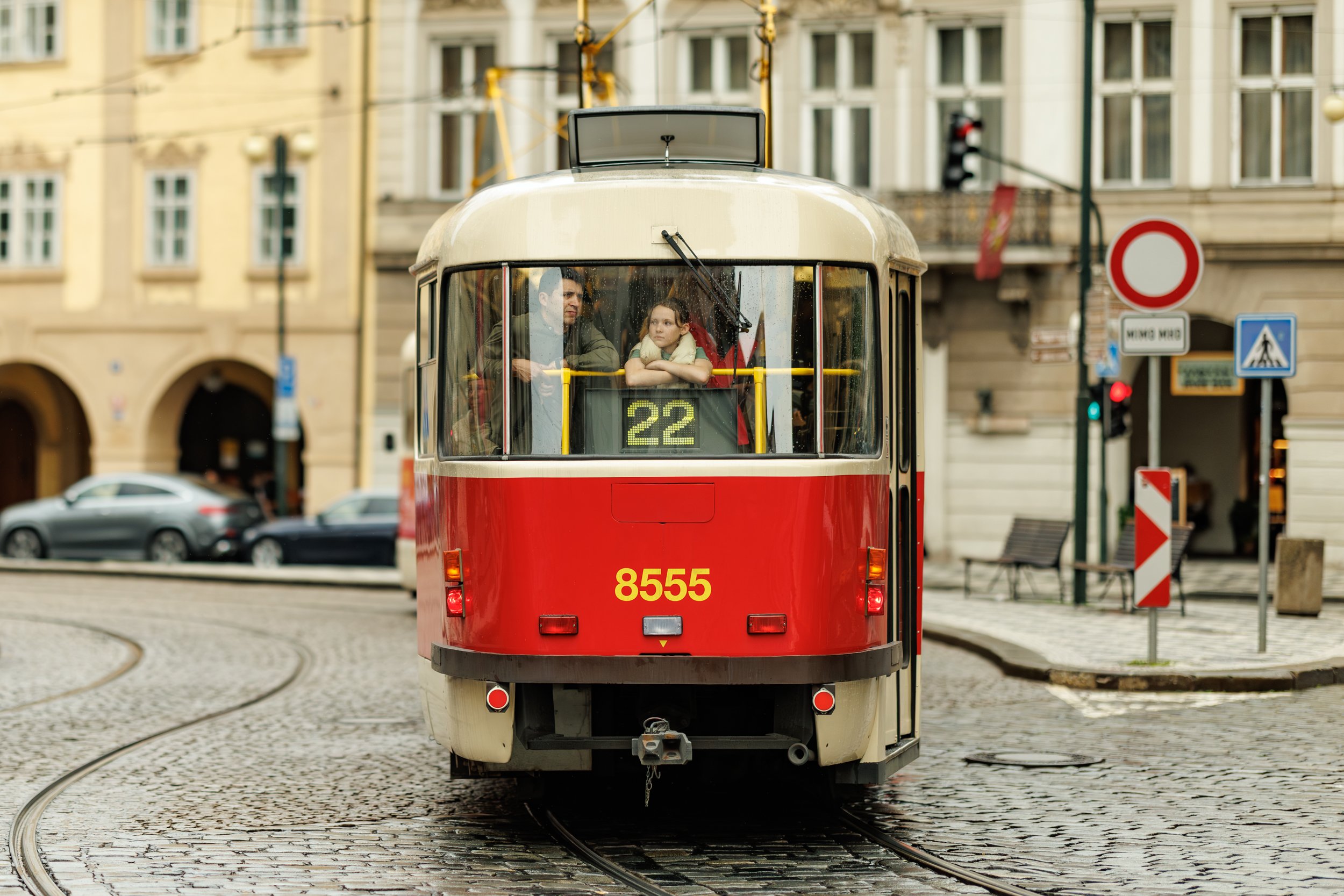 A red and cream-colored tram with the number 22 and the number 8555 on the front, moving on tracks in a city street with buildings, parked cars, and traffic signs visible in the background.