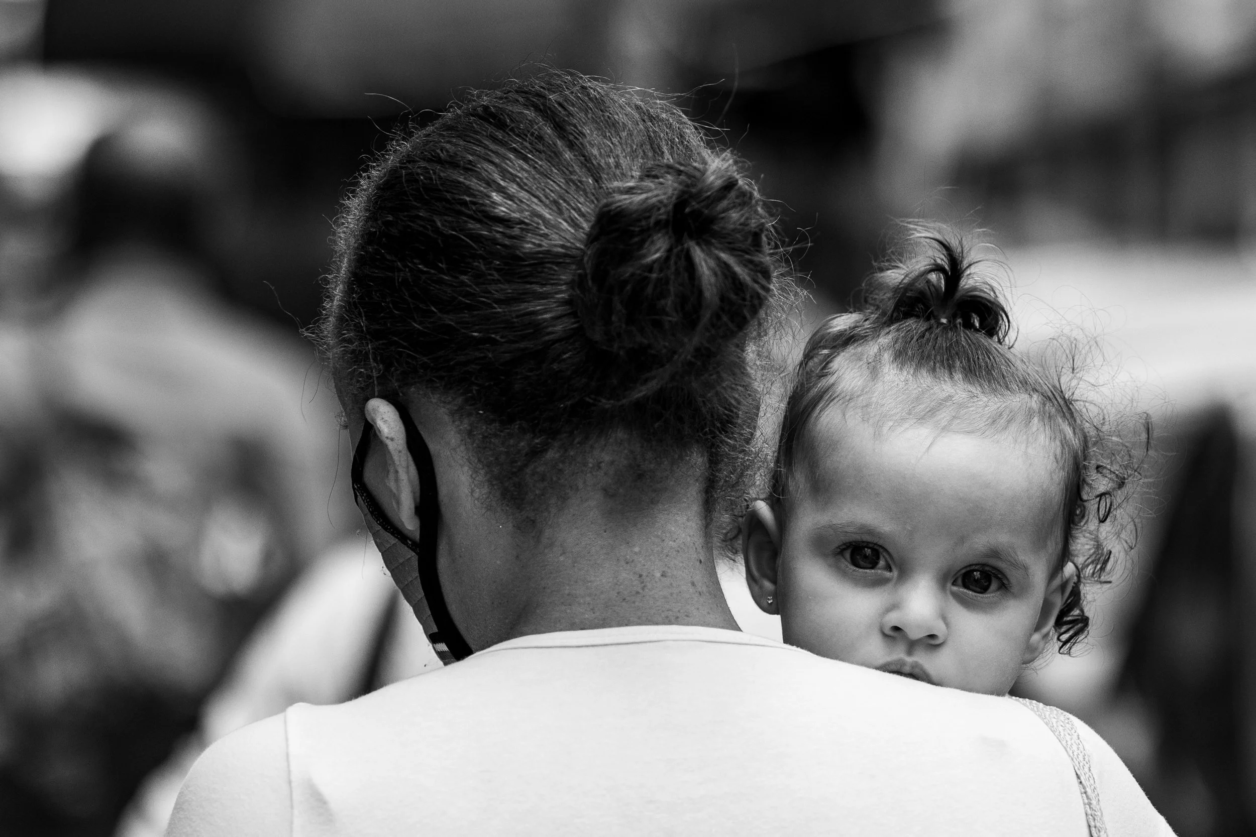 A person with glasses holding a young girl with dark curly hair, looking directly at the camera, in black and white.