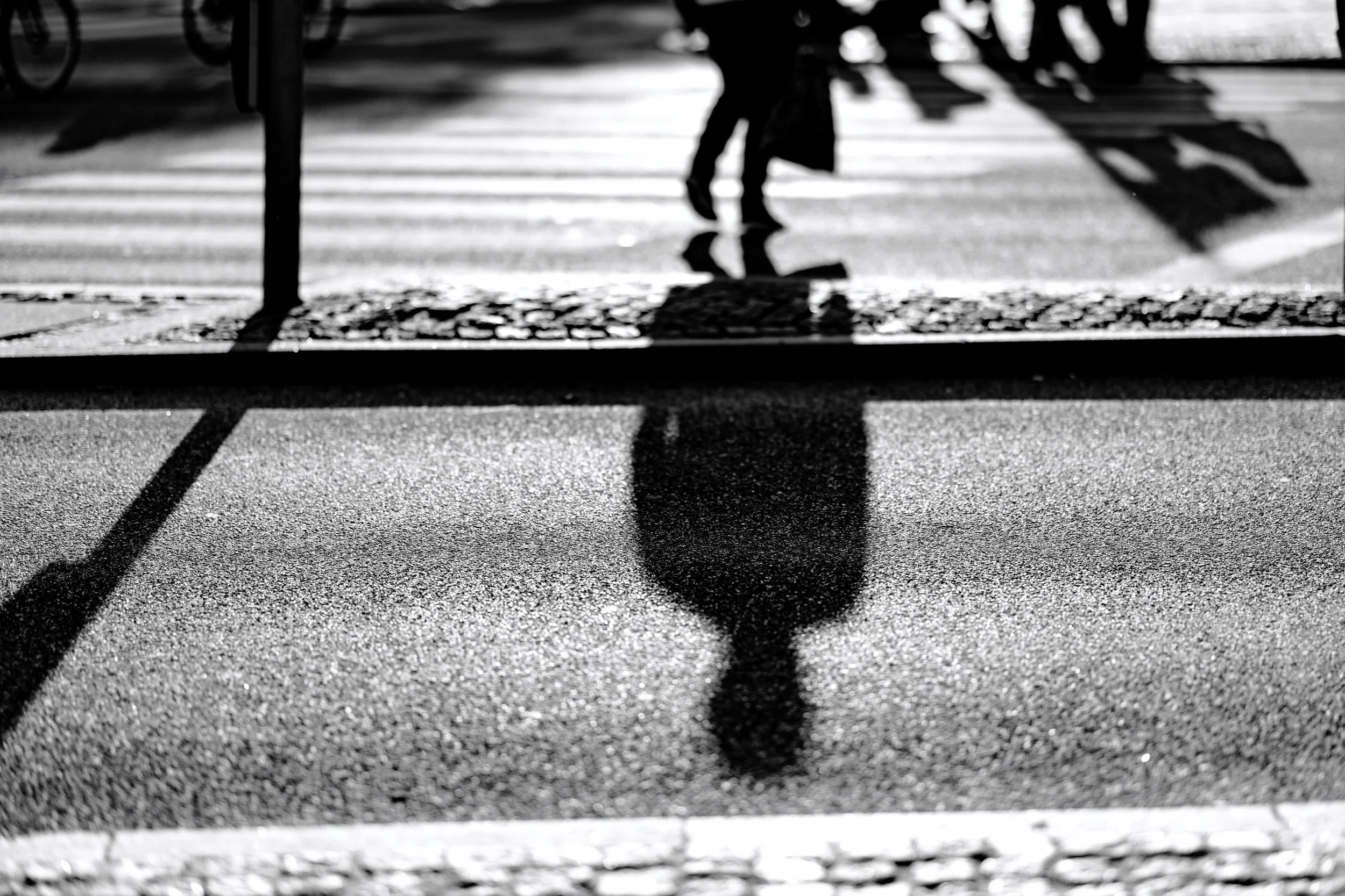 Black and white photo of a person walking on a crosswalk, casting a shadow on the street.