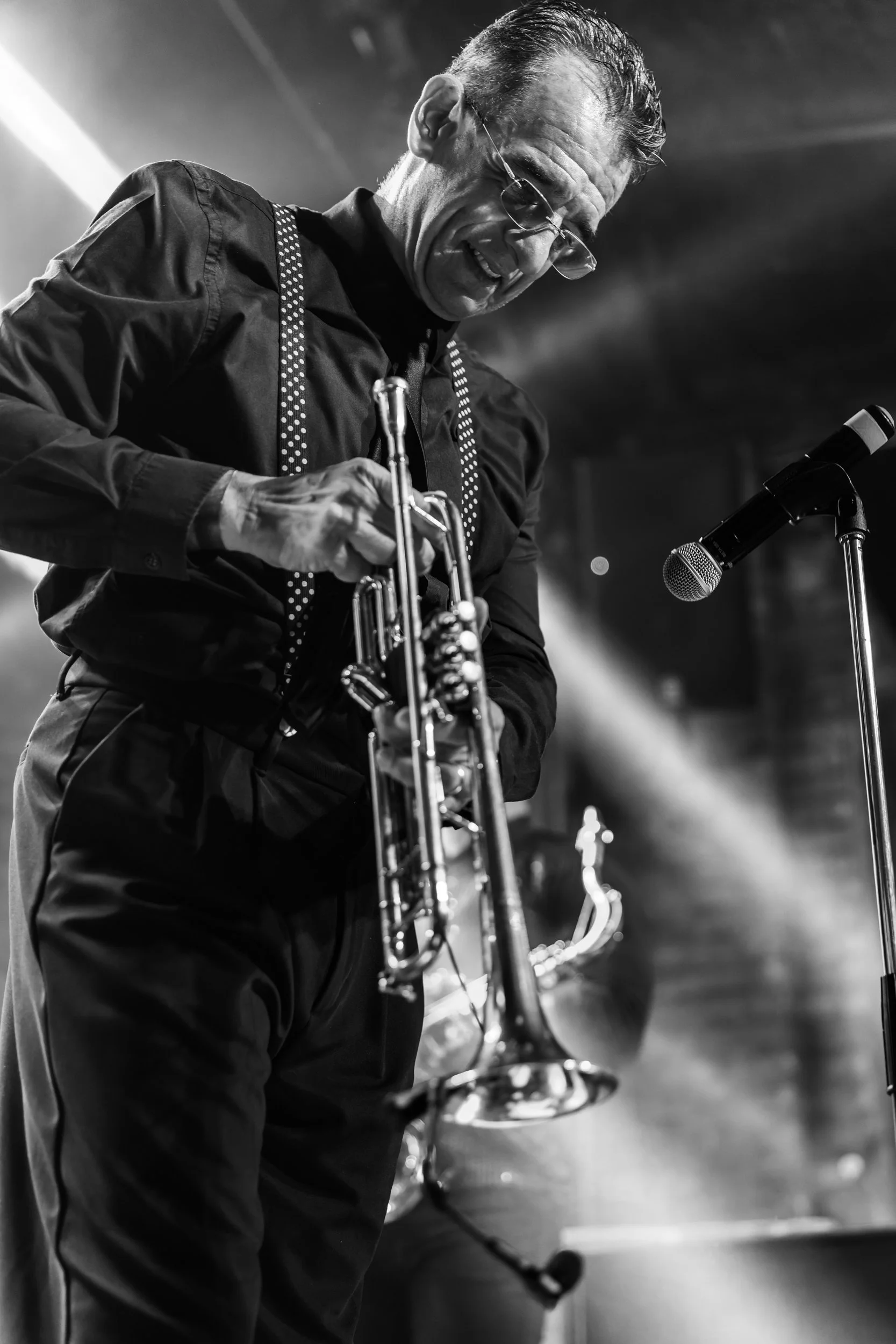 Black and white photo of a man playing a trumpet with a microphone in front of him, with a focused expression.