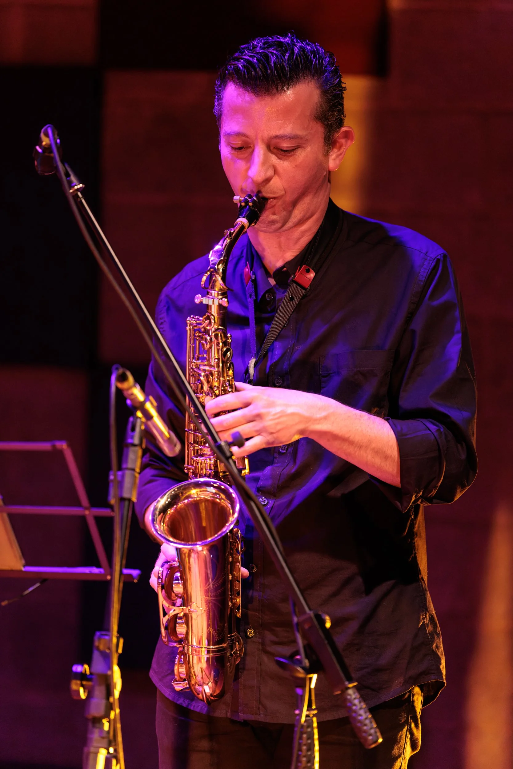 A man playing a gold saxophone in a dimly lit room with purple and orange lighting.