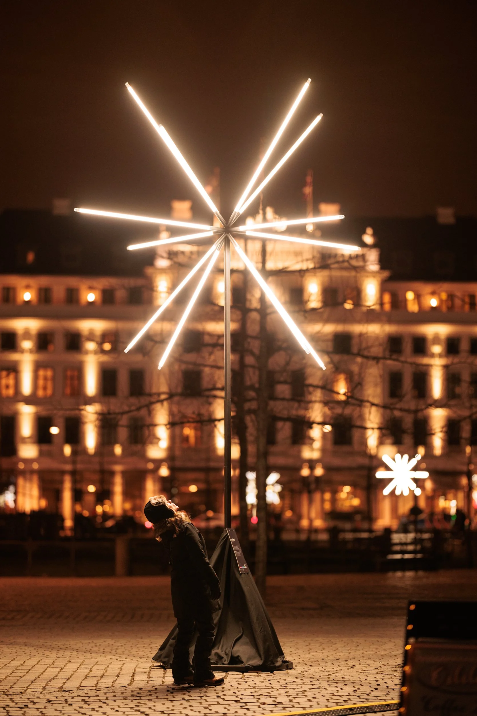 A person standing outdoors at night near a large, illuminated star-shaped decoration, with a building in the background lit by warm lights.