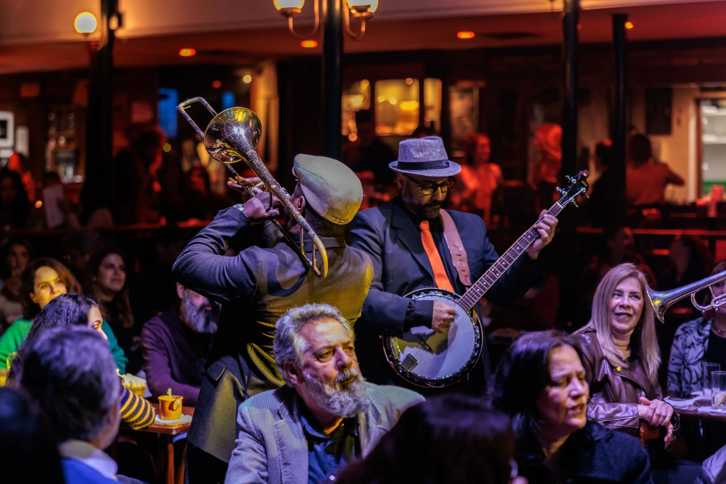 Musicians performing at a lively indoor event, with the audience seated at tables and decorated with warm lighting in the background.