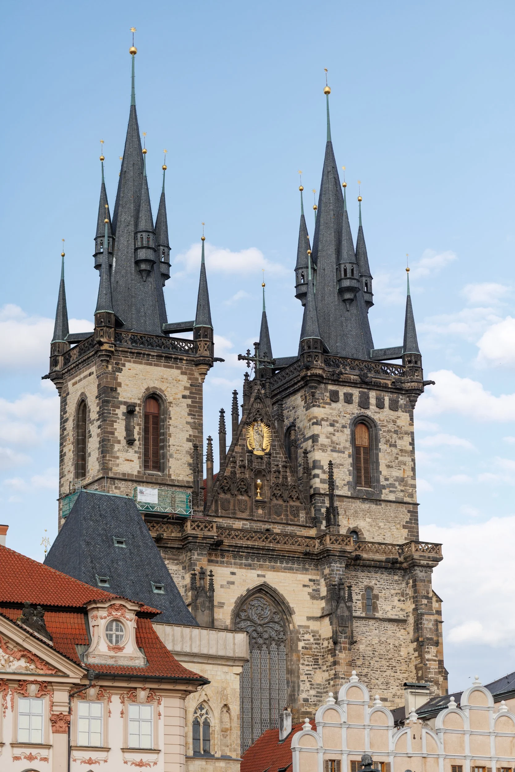 A historic Gothic-style church with multiple tall pointed spires topped with golden spheres and stars, set against a partly cloudy sky. The church has an ornate facade with large stained glass windows and decorative elements.