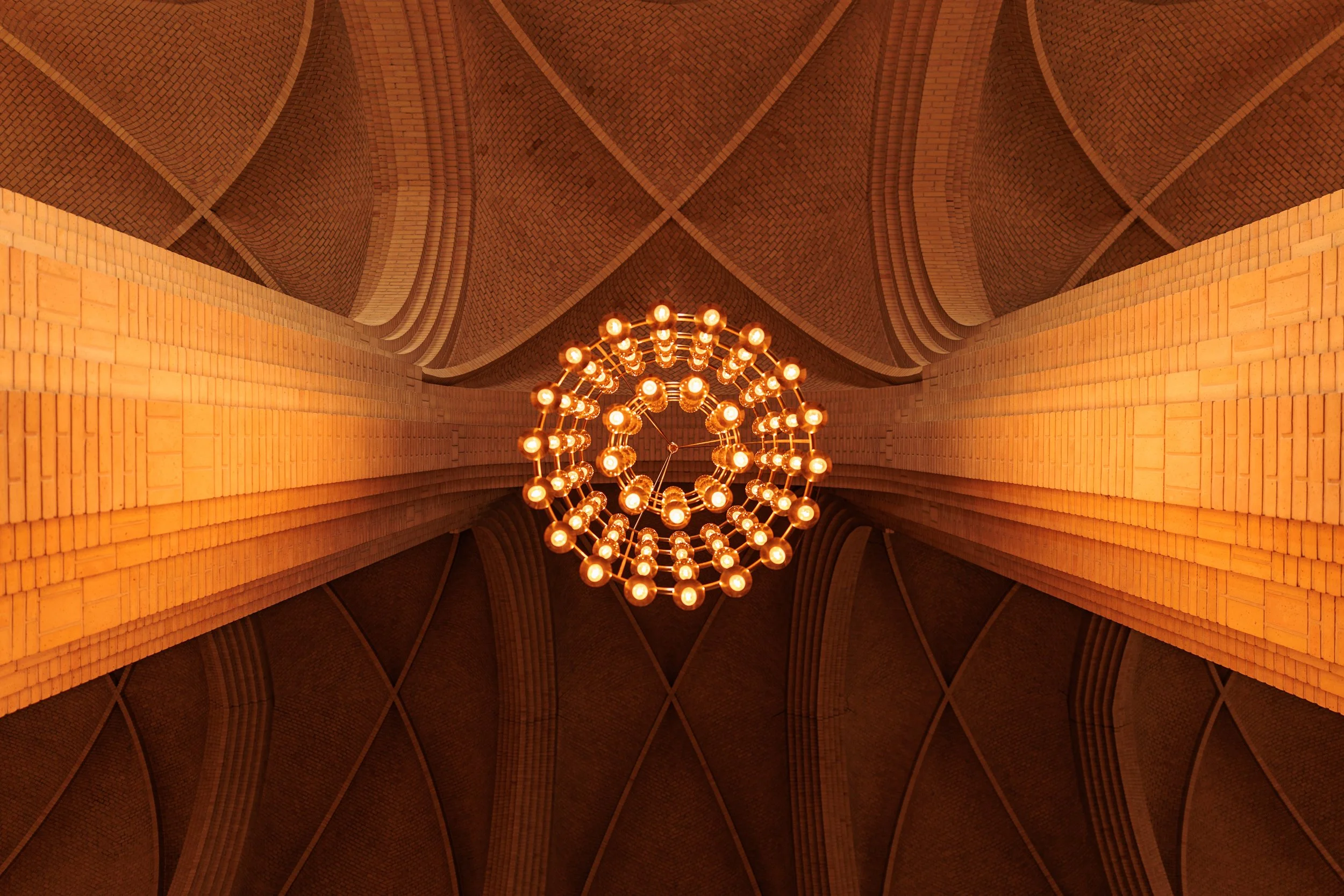 Interior view of a brick vaulted ceiling with a large, modern, circular chandelier hanging from the center.