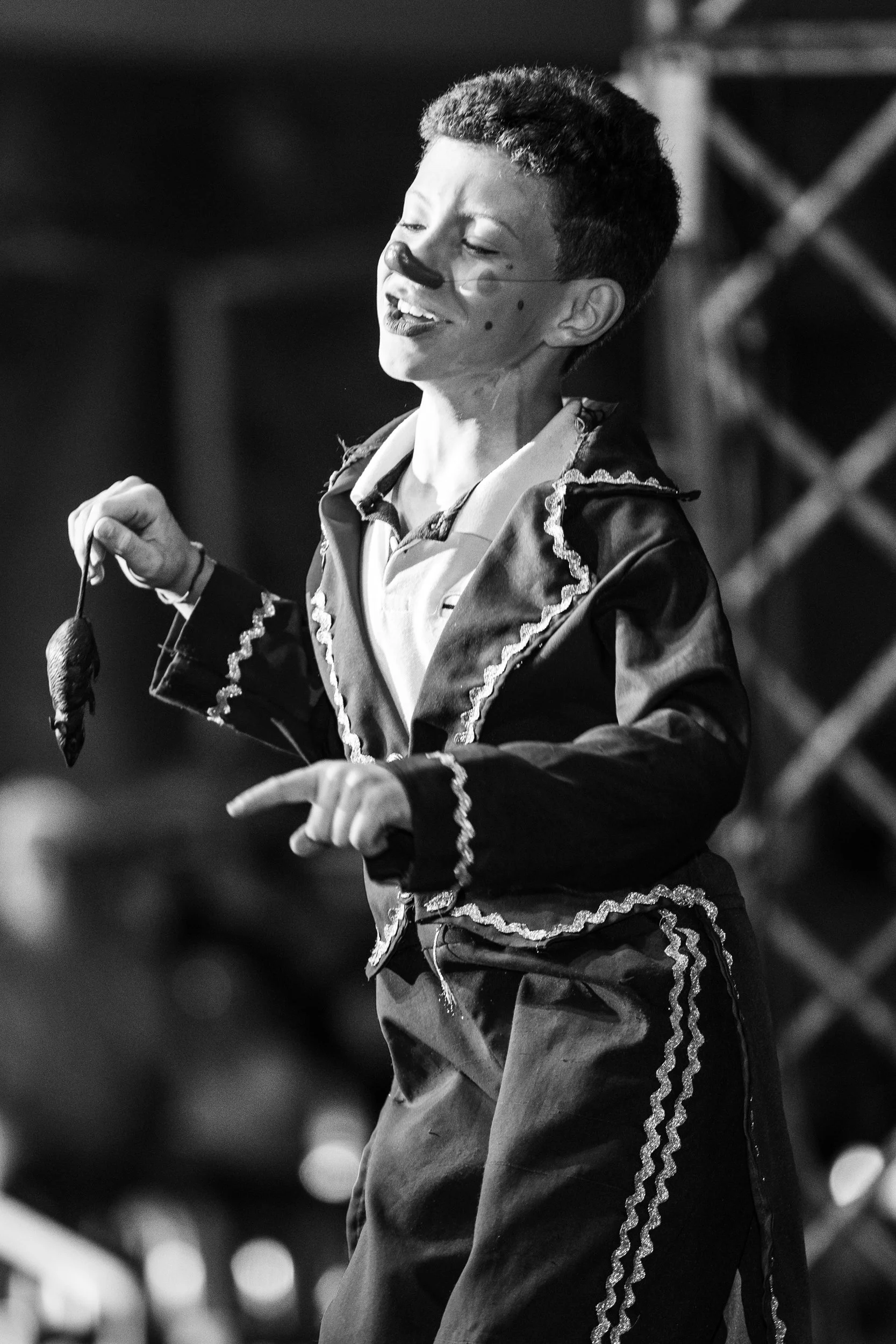 A performer with face paint, wearing a costume with decorative stitching, singing or speaking into a microphone on stage.