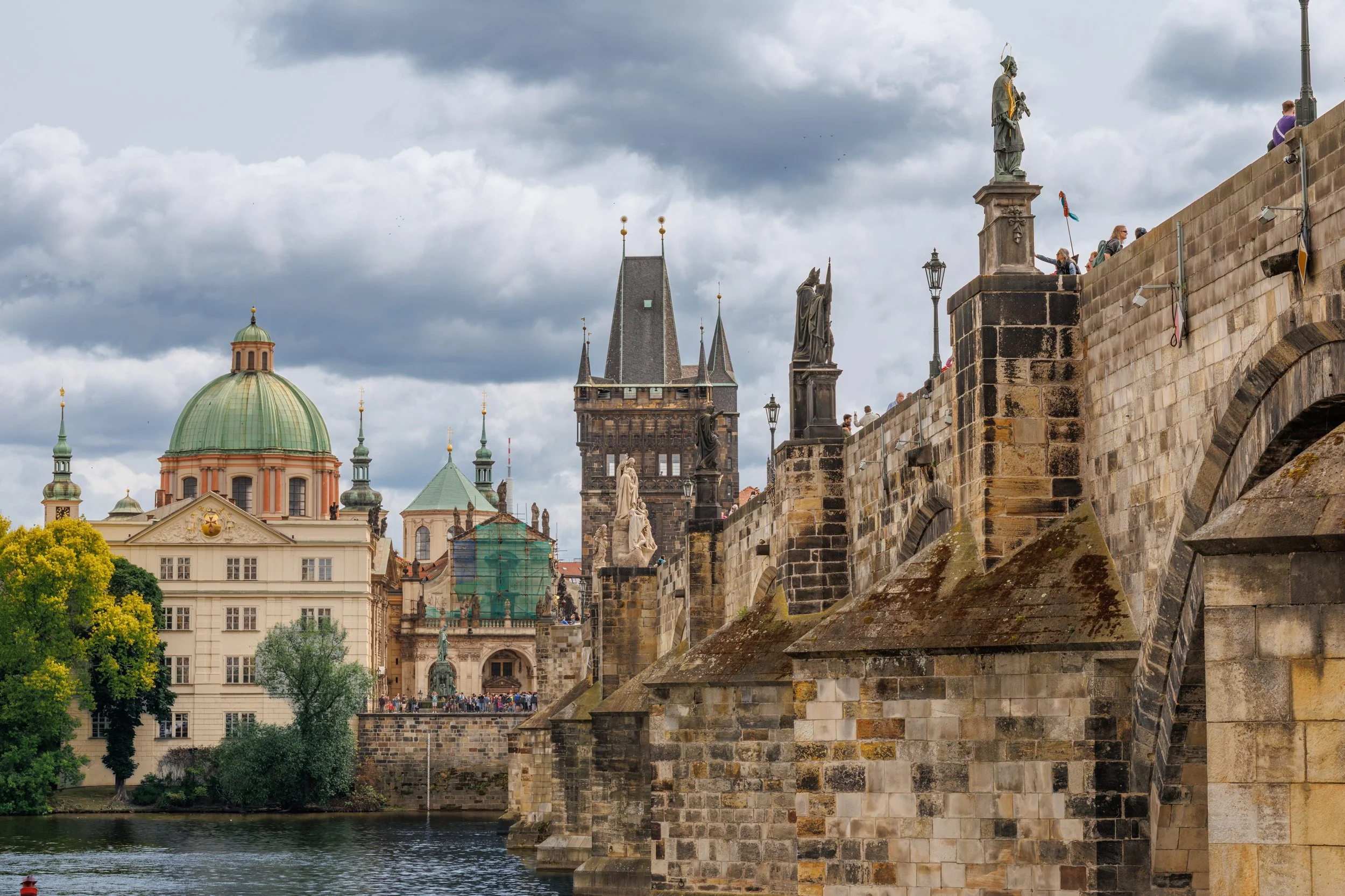View of historic buildings and statues along the Charles Bridge in Prague, Czech Republic, with cloudy sky overhead.