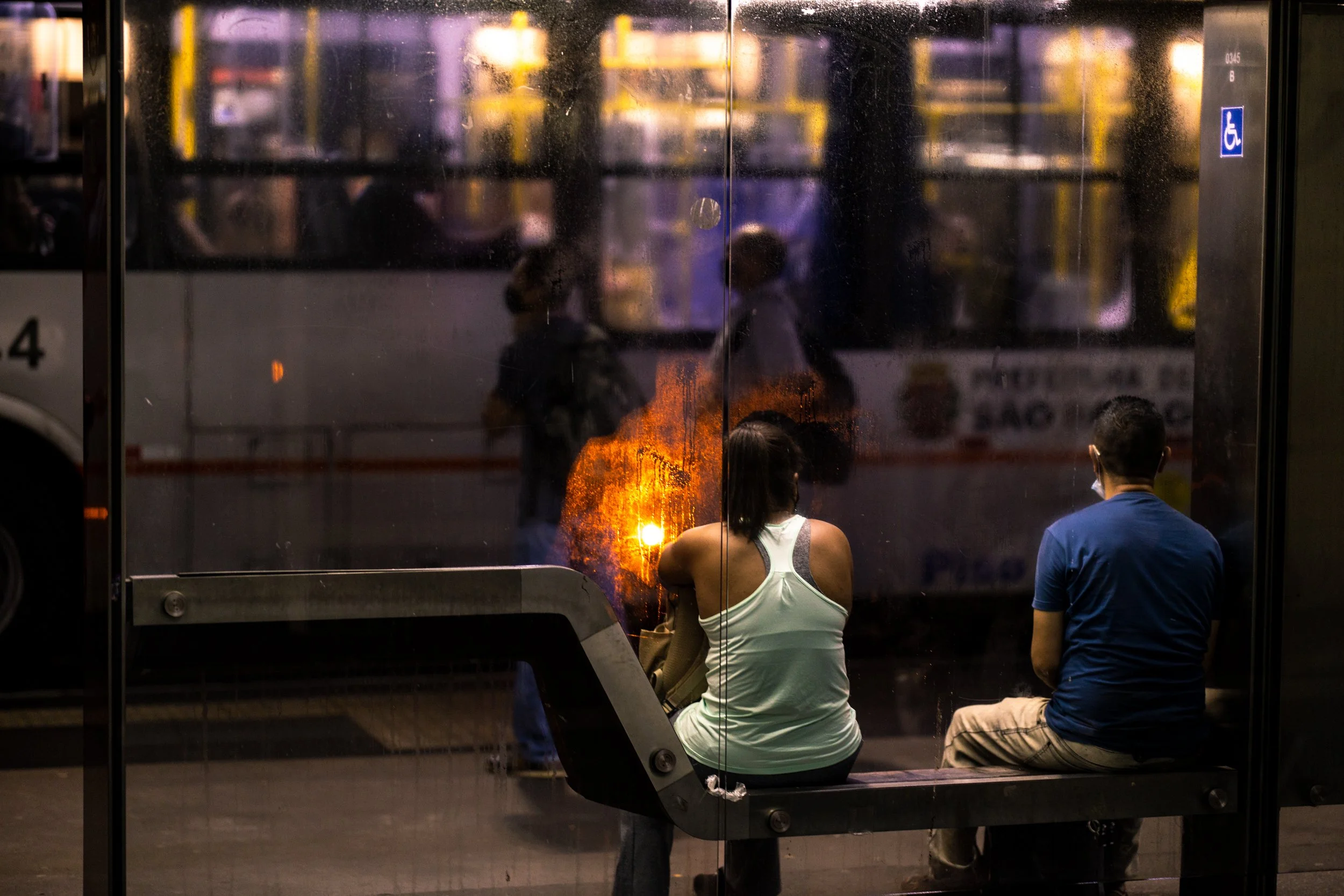 People sitting at a bus stop during a fire at night.