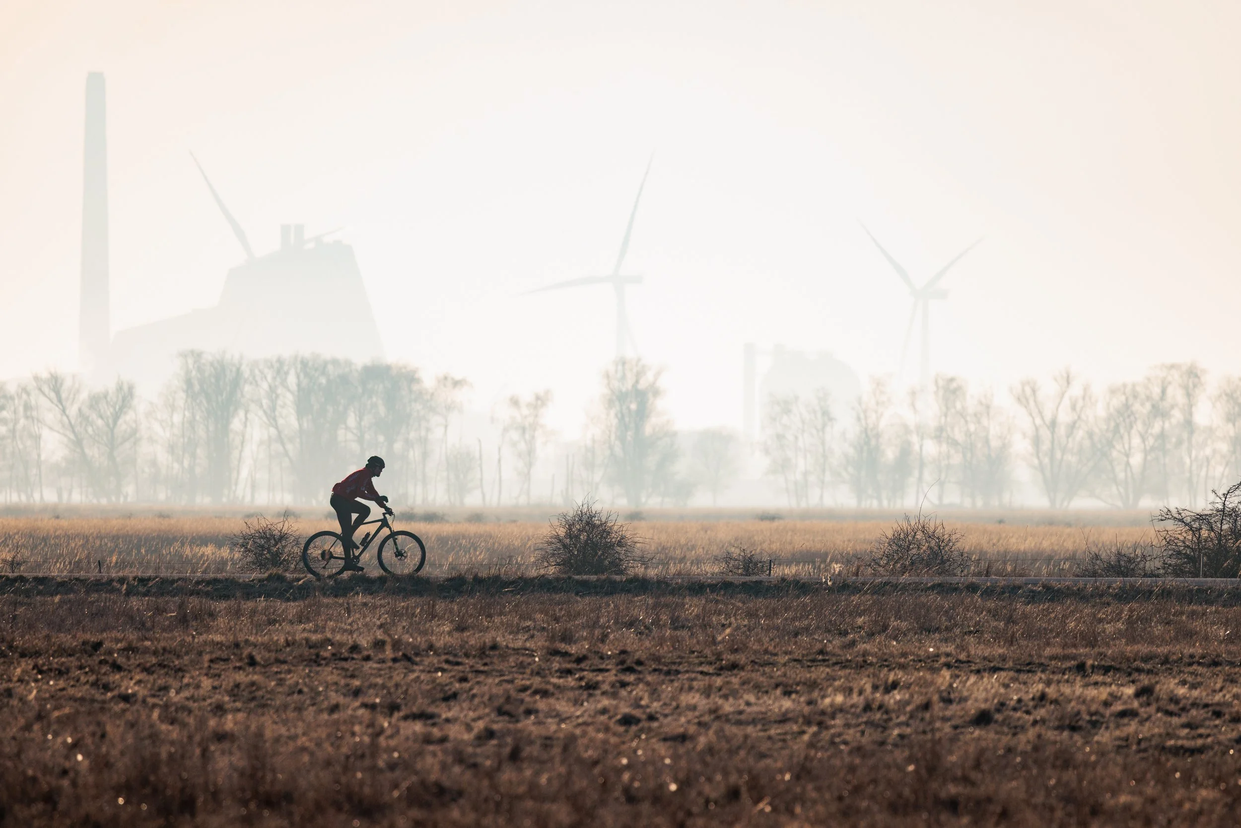 A person riding a bicycle across a field with wind turbines in the background.
