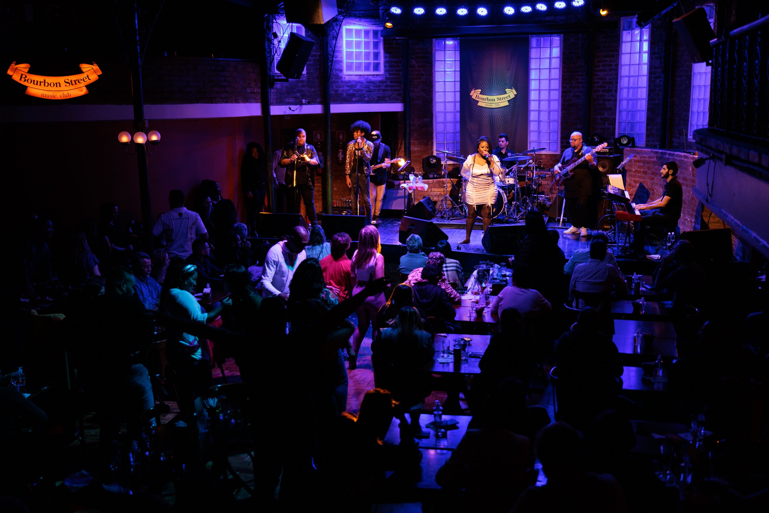 Live music performance at Bourbon Street music club with a band on stage and an audience in the foreground.