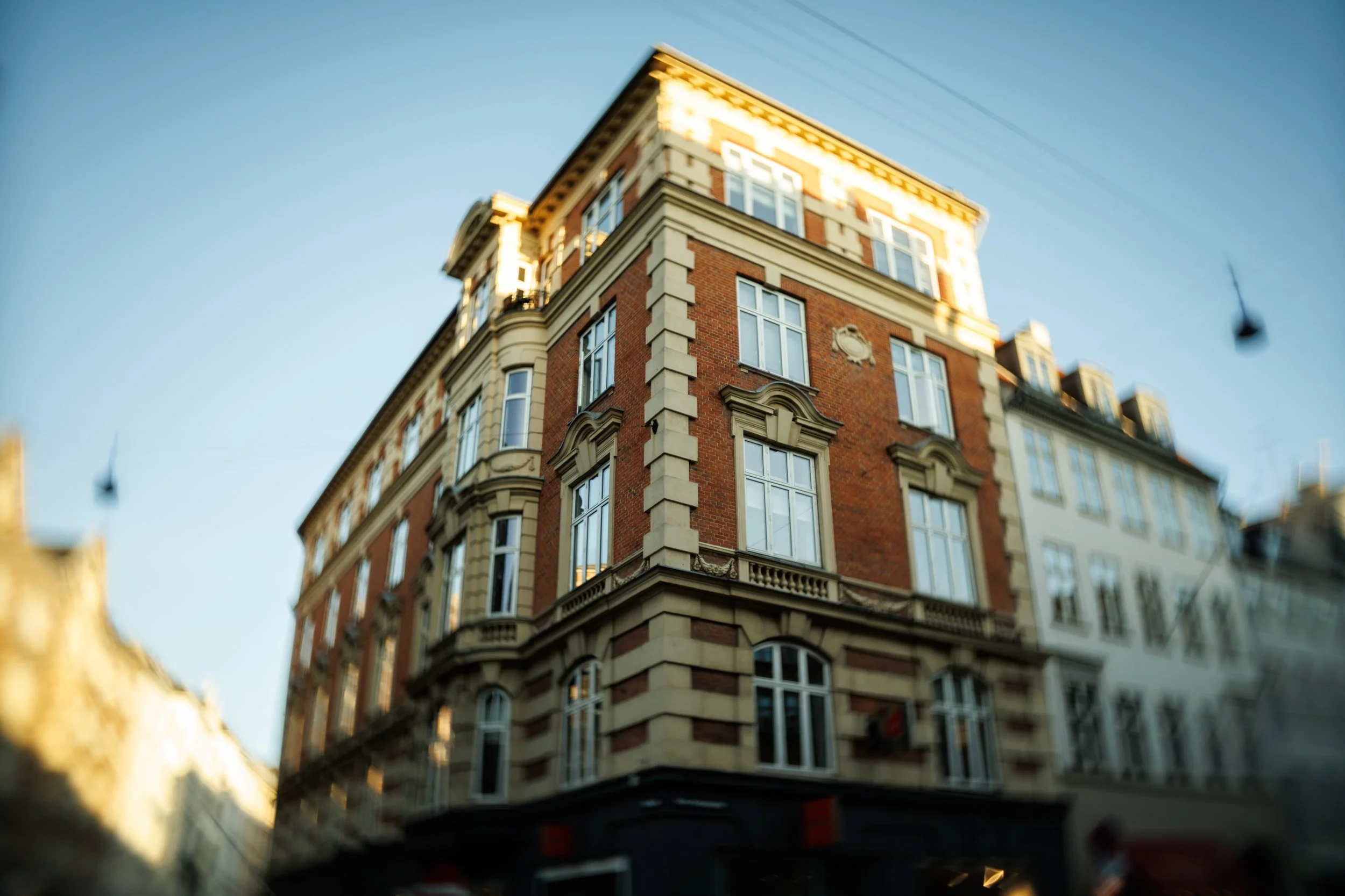 A multi-story brick and cream-colored building with large windows and ornate architectural details, viewed from below against a clear blue sky.