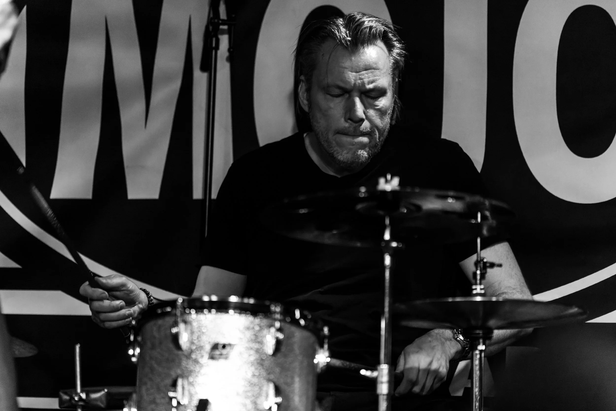 Black and white photo of a man with his eyes closed, playing drums.