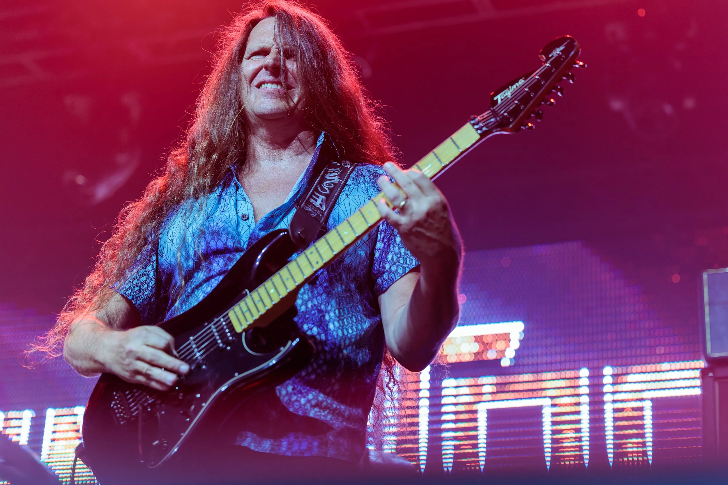 A woman playing an electric guitar on stage with colorful lighting and LED screens in the background.