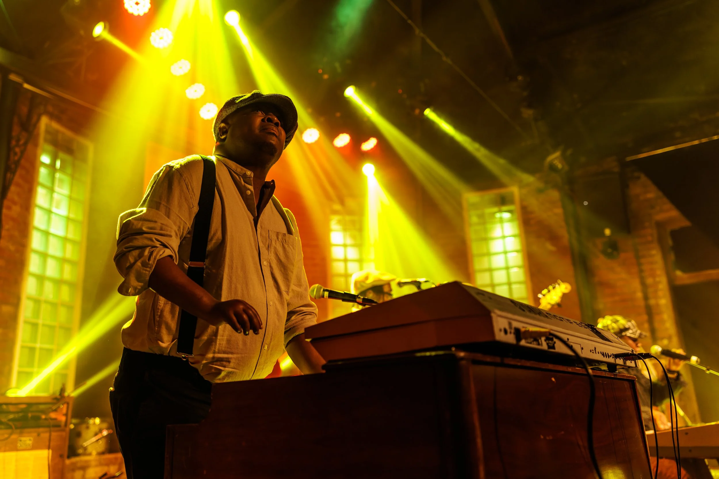 A musician playing keyboard on stage with bright yellow and green stage lighting