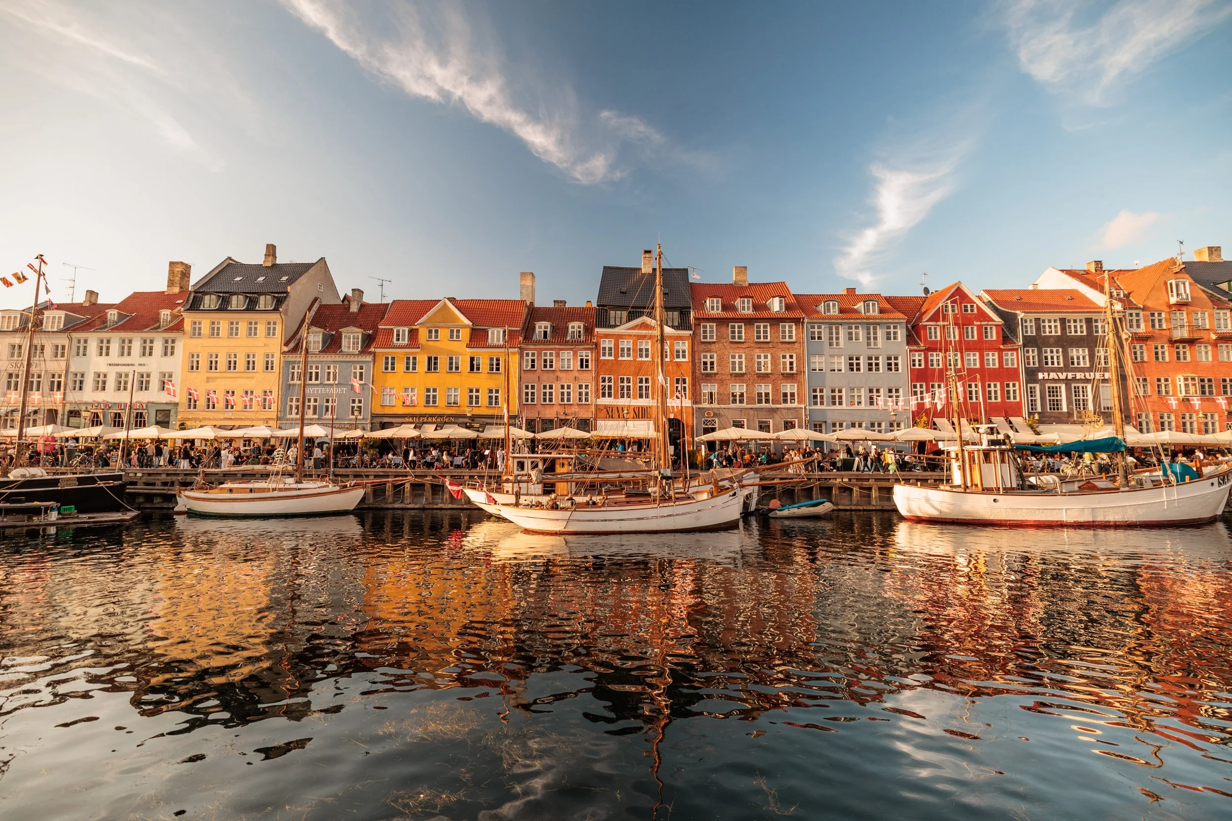 Colorful row of houses along a waterfront with boats docked in the harbor and a blue sky with clouds.