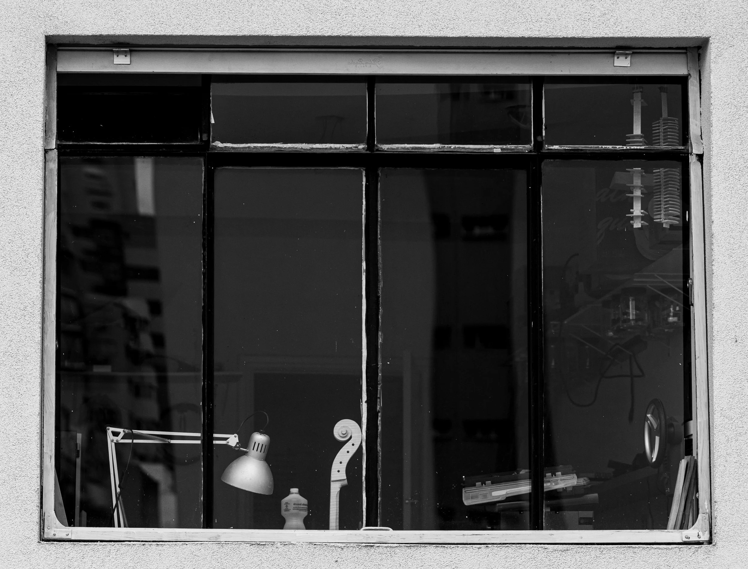 Black and white photo of a window with several items inside including a desk lamp, a bottle, and decorative objects.