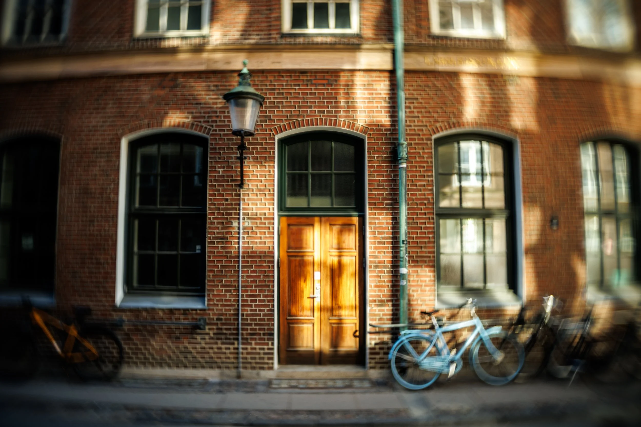 A brick building facade with multiple windows, a wooden door, a street lamp, and bicycles parked in front.