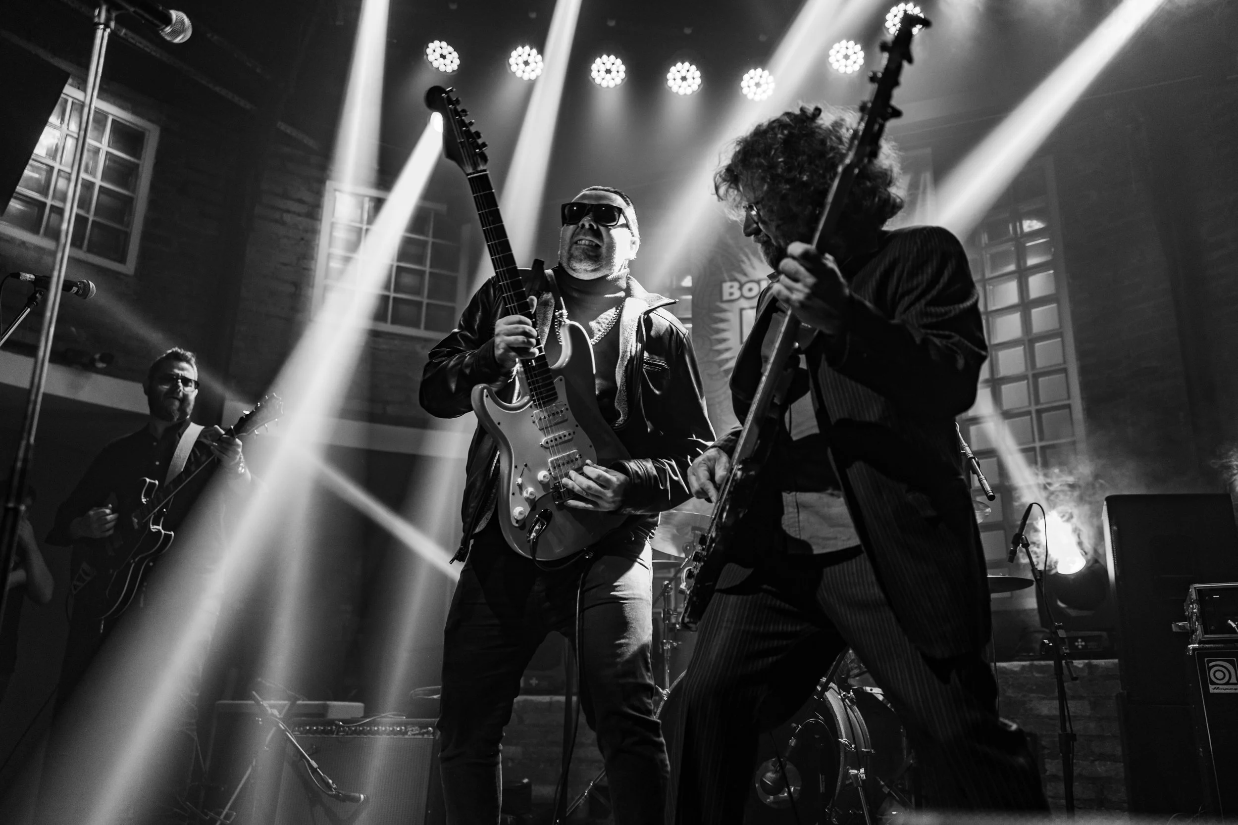 Musicians performing on stage with guitars under bright spotlights, black and white photo.