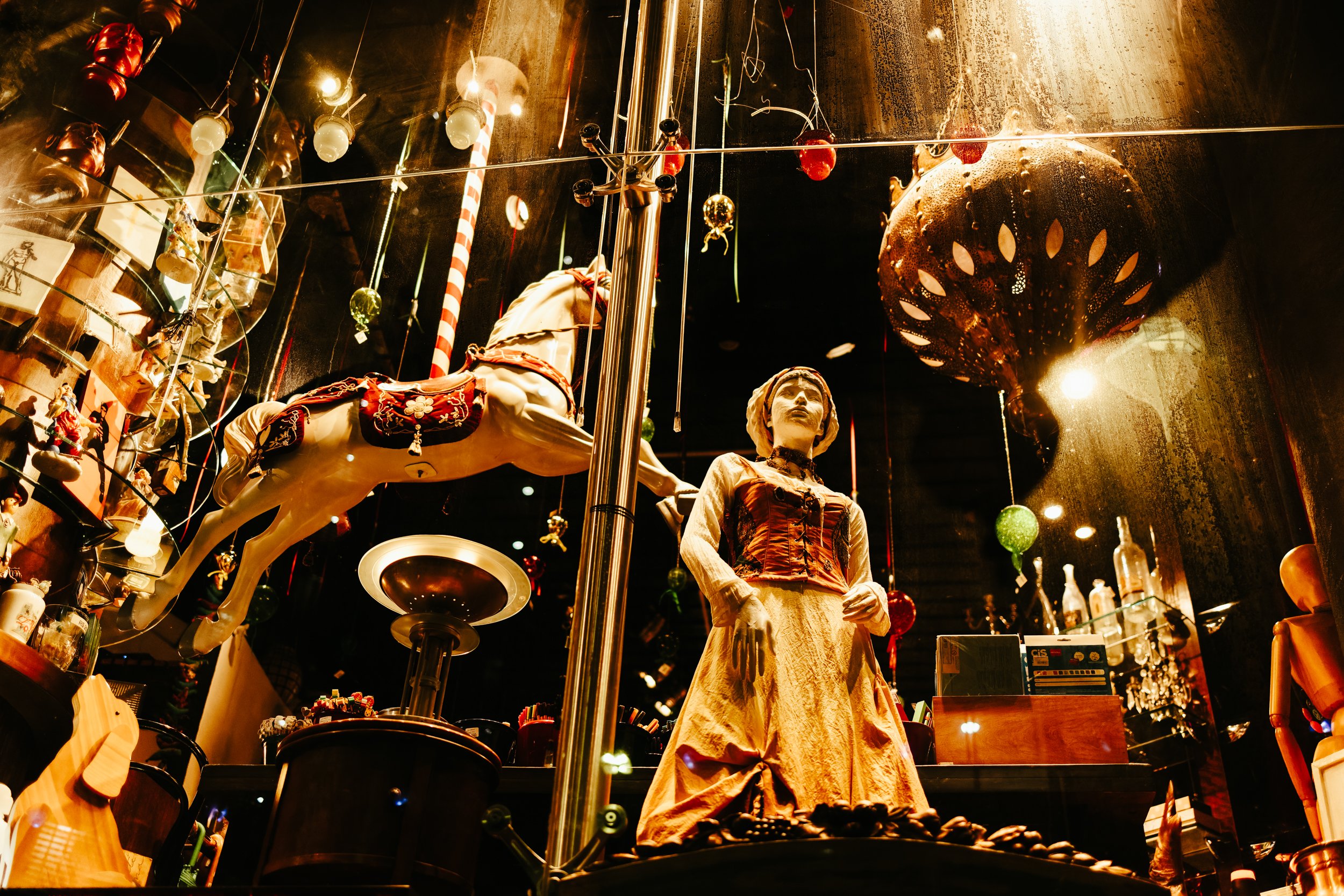 A display of vintage toys and collectibles including a figurine of a woman in a dress, a toy horse, Christmas ornaments hanging from the ceiling, and other decorative items in a dimly lit store.