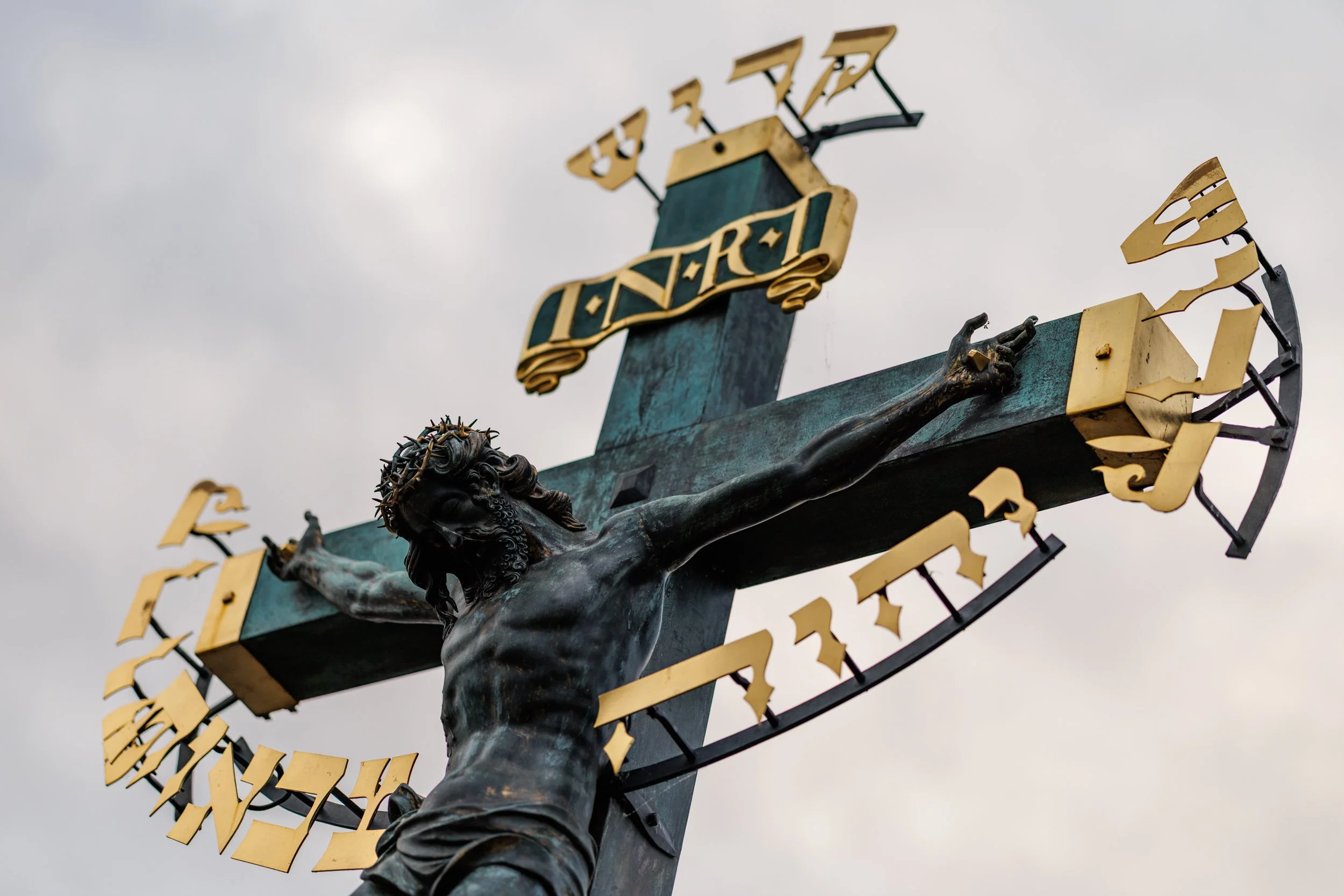 Close-up of a religious sculpture of Jesus Christ on the cross, with a crown of thorns on his head, against a cloudy sky.