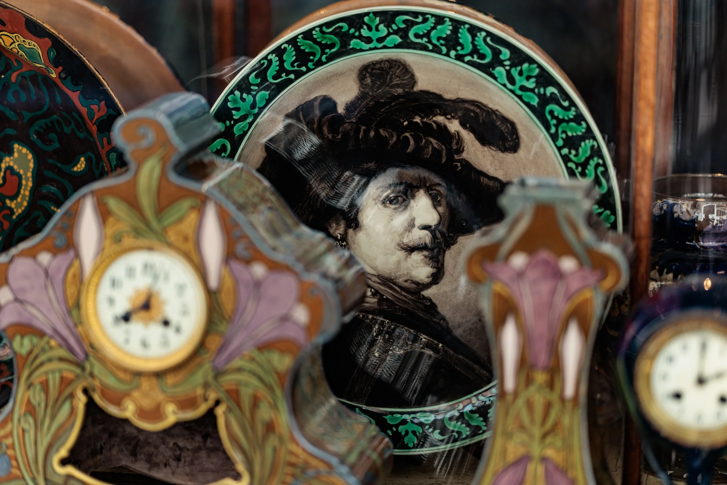 Various decorative porcelain plates with intricate designs, including one with a black and white portrait of a man with a headband, surrounded by green leafy patterns, and other colorful floral patterns.