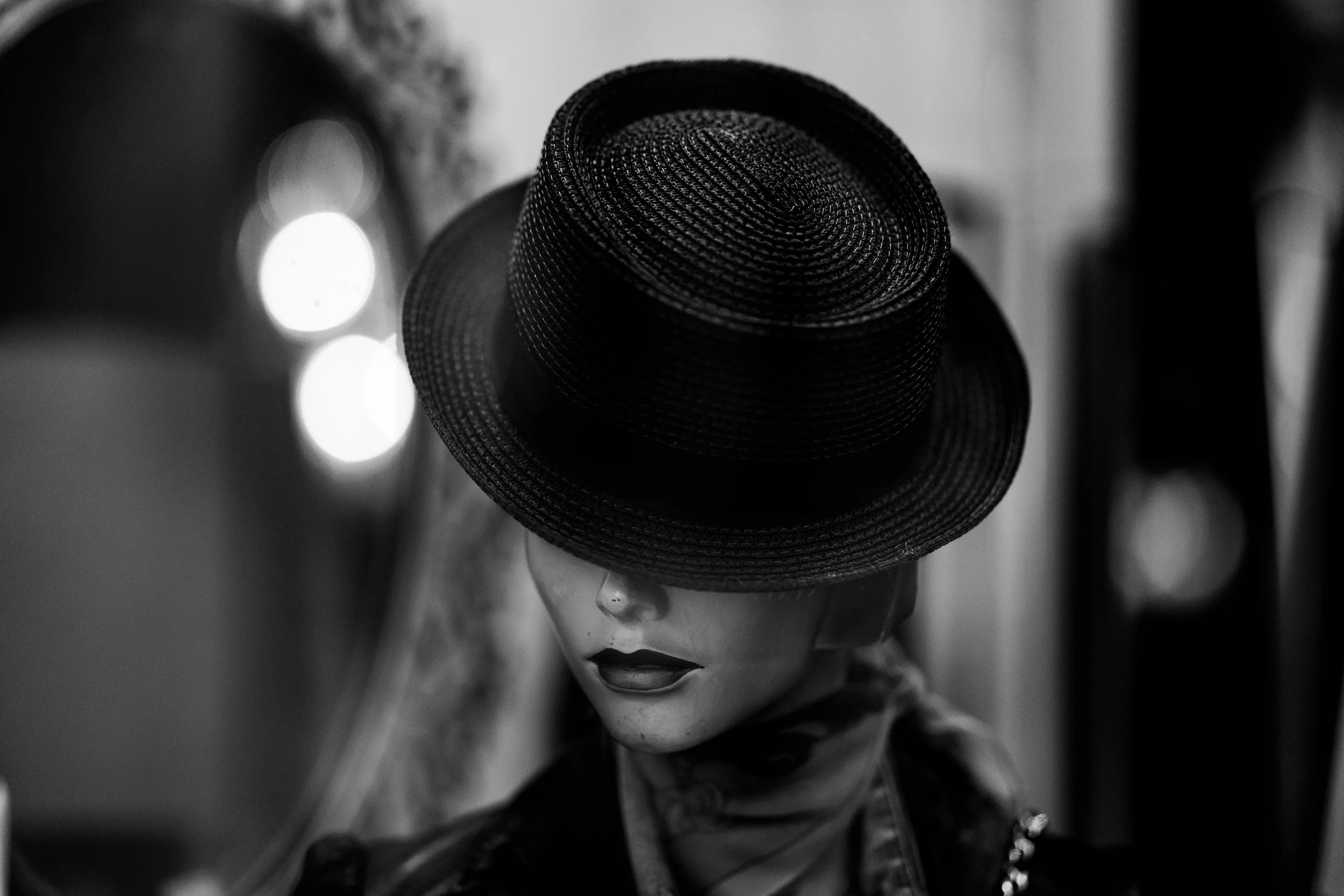A mannequin head wearing a wide-brimmed, textured black hat with the brim tilted downward. The image is in black and white, with soft lighting highlighting the hat's woven pattern and the mannequin's facial features.