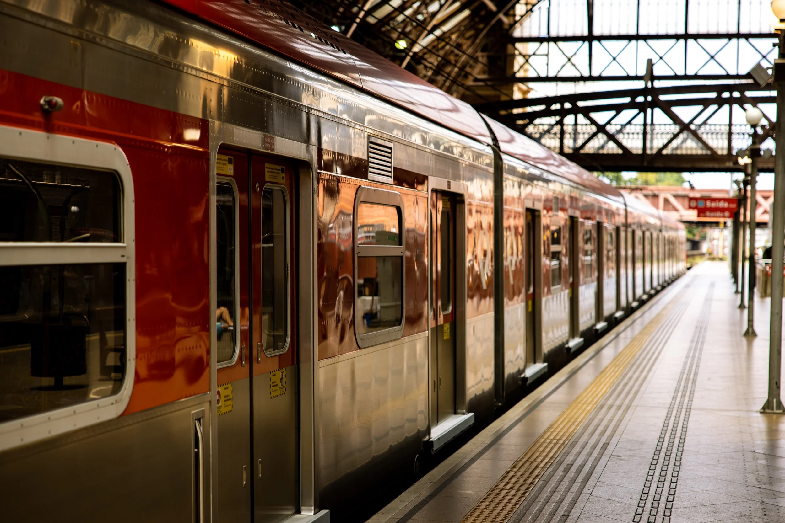 An orange and silver train at a train station platform with a covered roof overhead.