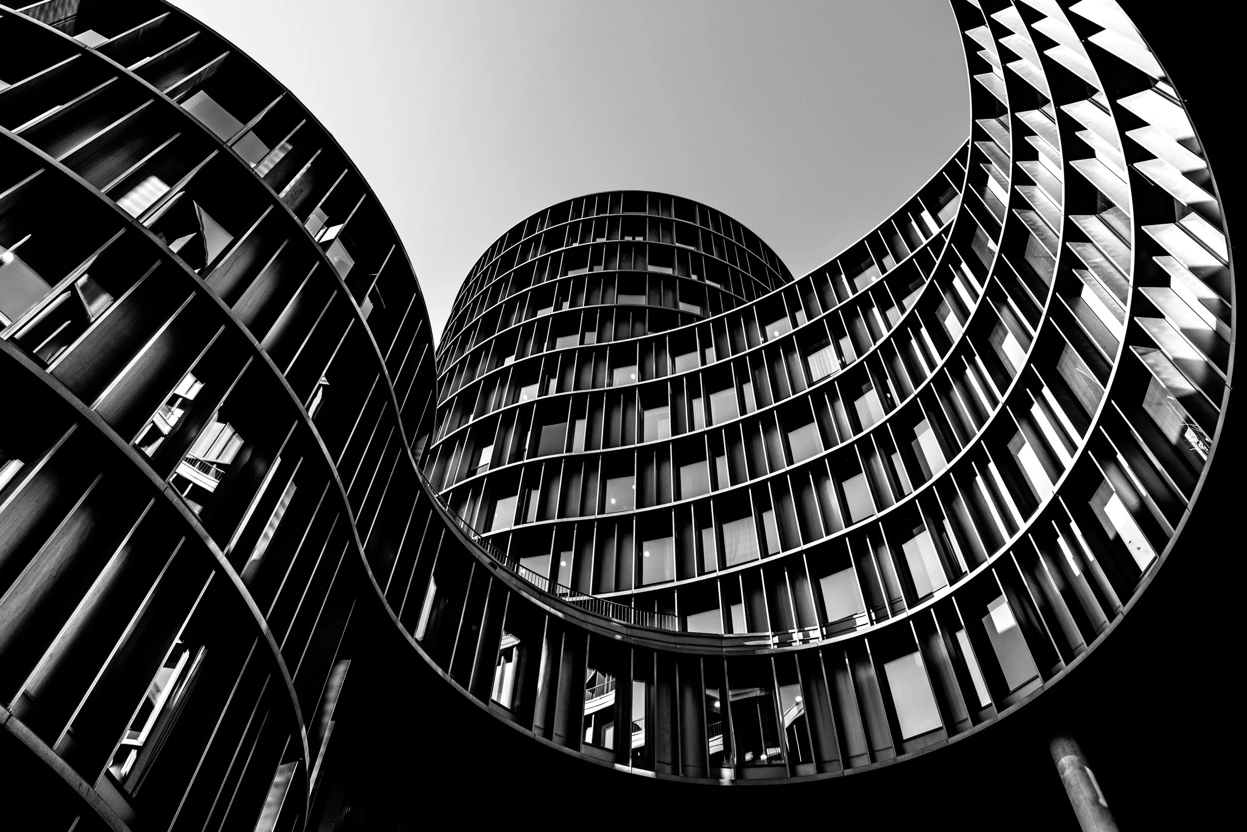 Black and white photo of a modern spiral building taken from below, showcasing its curved balconies and glass windows.