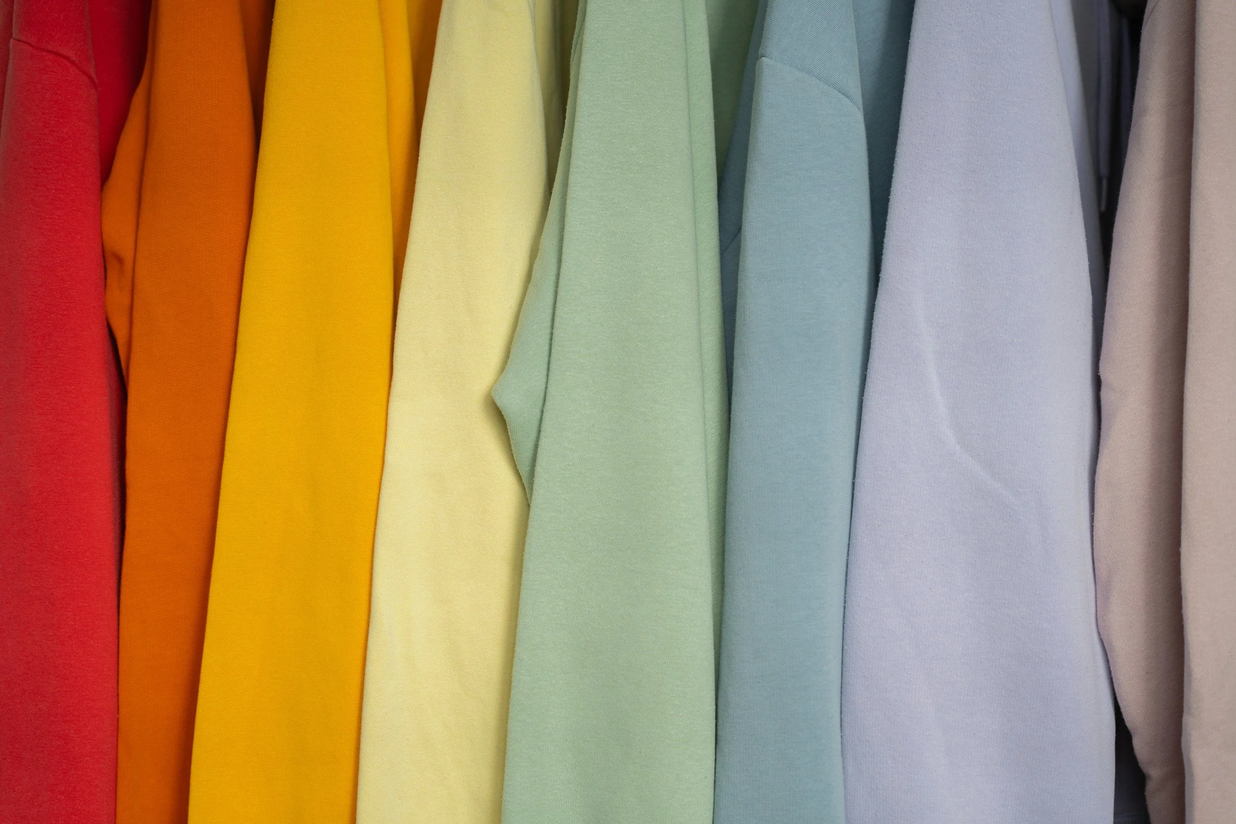 Colorful shirts arranged in a rainbow spectrum from red to beige.
