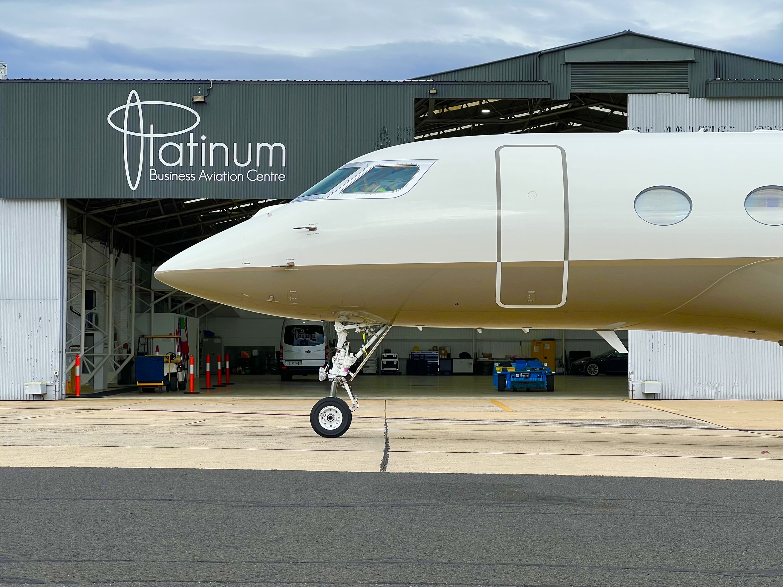 Front view of a commercial airplane parked at the runway in front of a green hangar building with 'Platinum Business Aviation Centre' written on it.