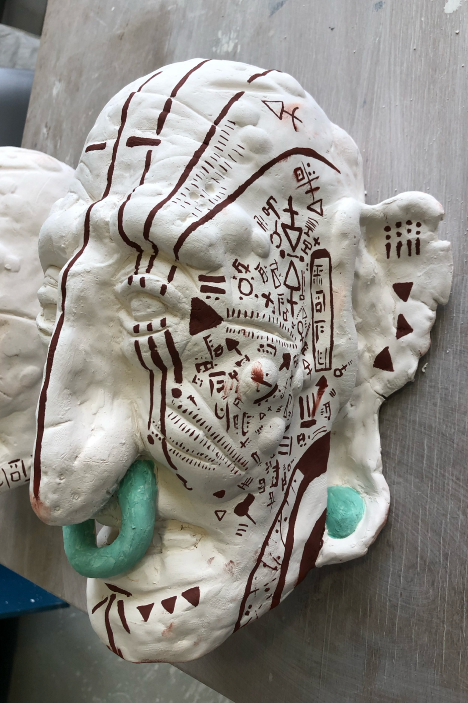 A realistic sculpture of a human brain with detailed markings and symbols, painted white with brown and teal accents, resting on a metallic surface.
