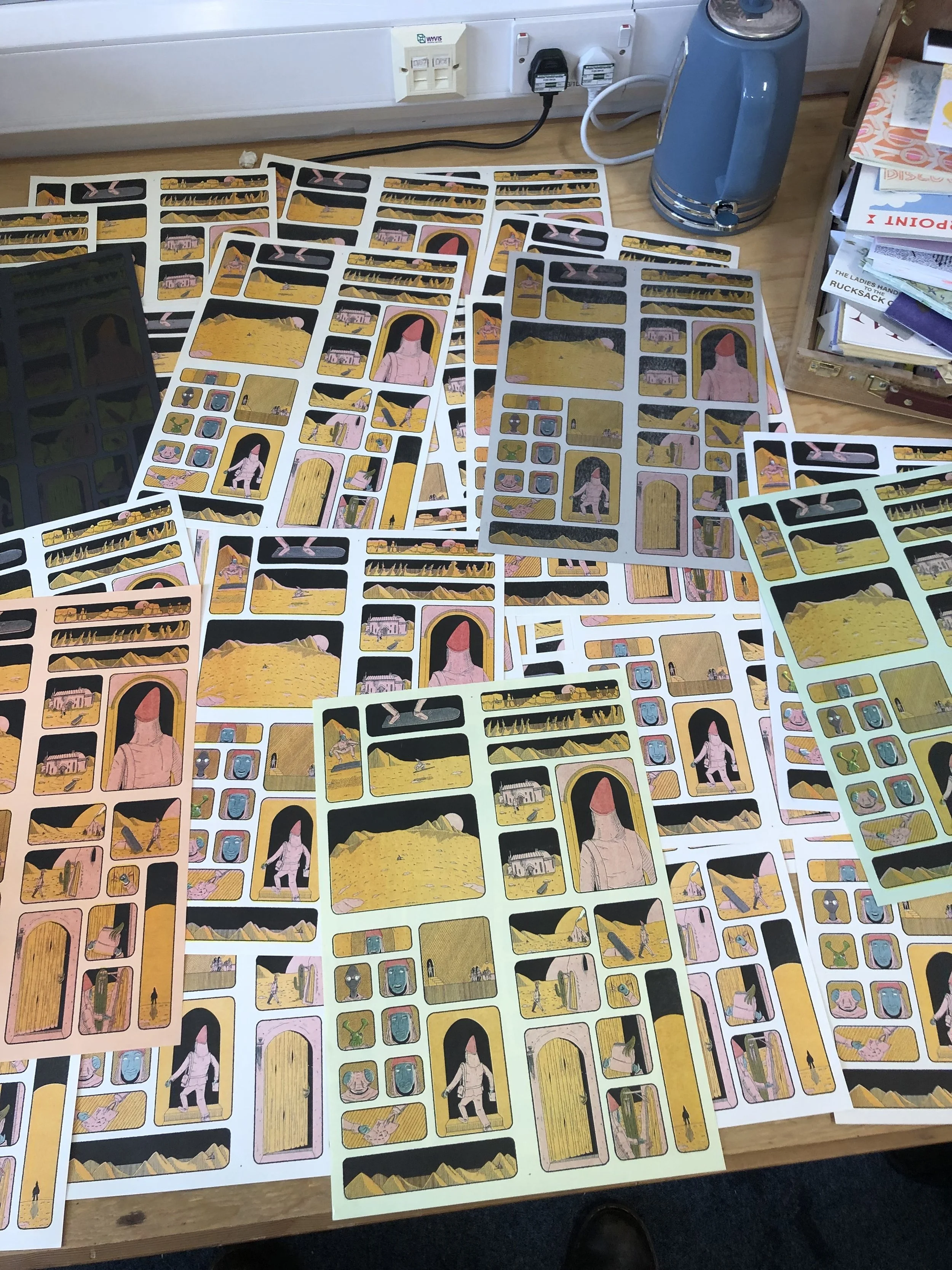 Multiple sheets of illustrated story cards spread out on a wooden table, depicting scenes with characters and scenery in a stylized, cartoonish art style.