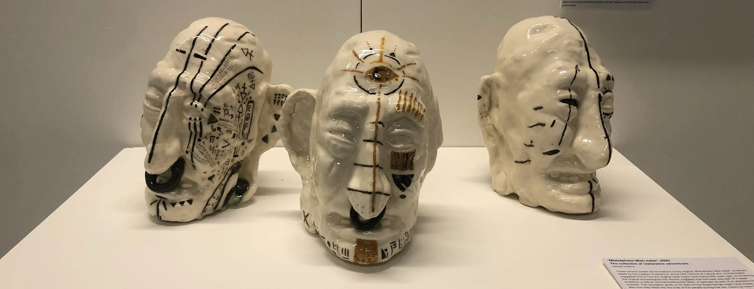 Three ceramic masks with abstract designs and markings, displayed on a white surface in a museum setting.