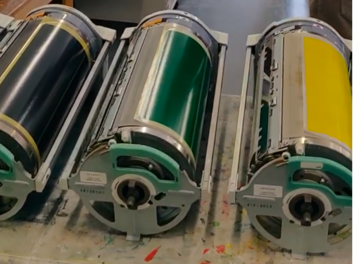 Three cylindrical color printing machines with black, green, and yellow ink colors.