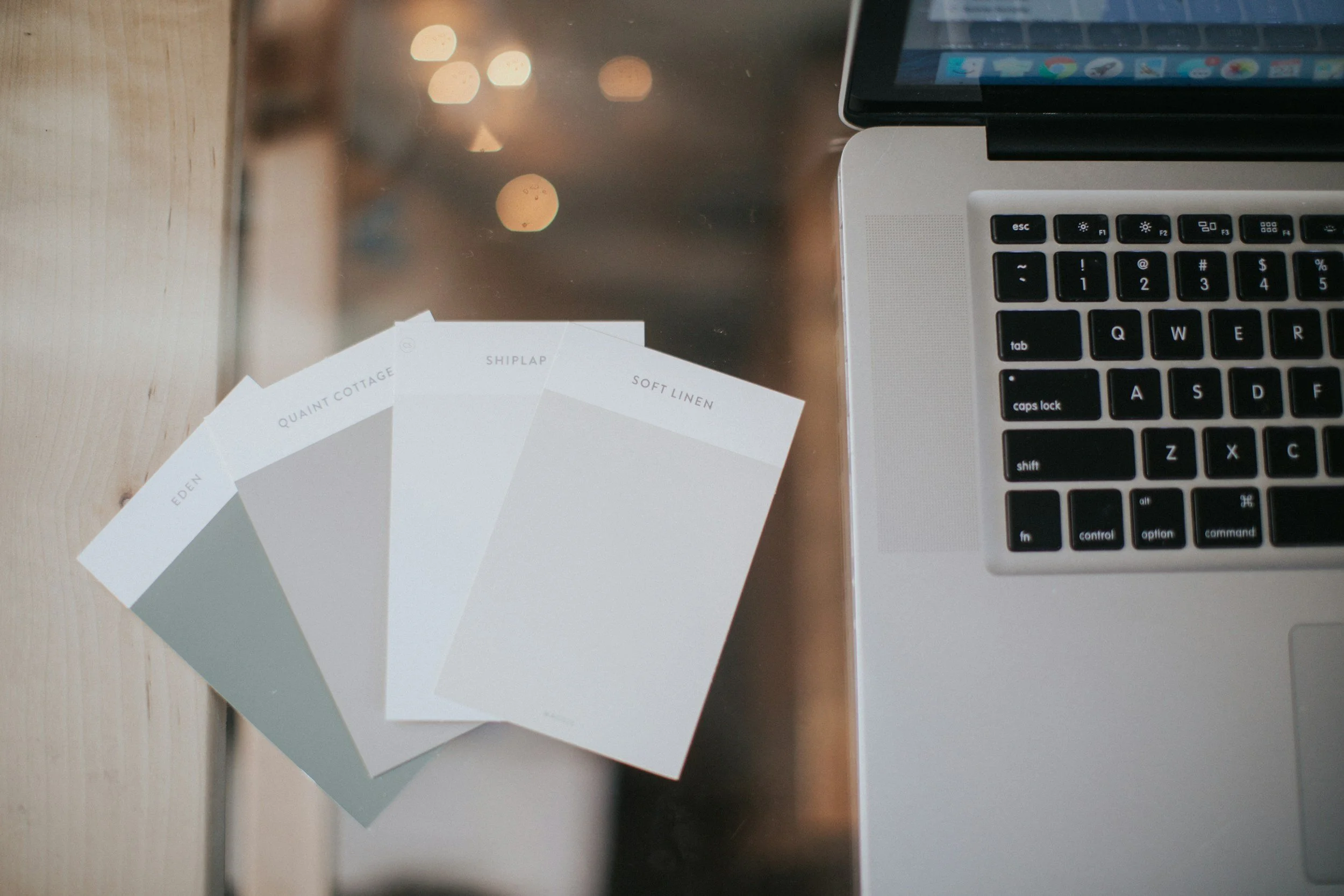 Color swatches labeled Eden, Quaint Cottage, Shiplap, Soft Linen on a wooden surface next to a laptop with a silver body and black keyboard.
