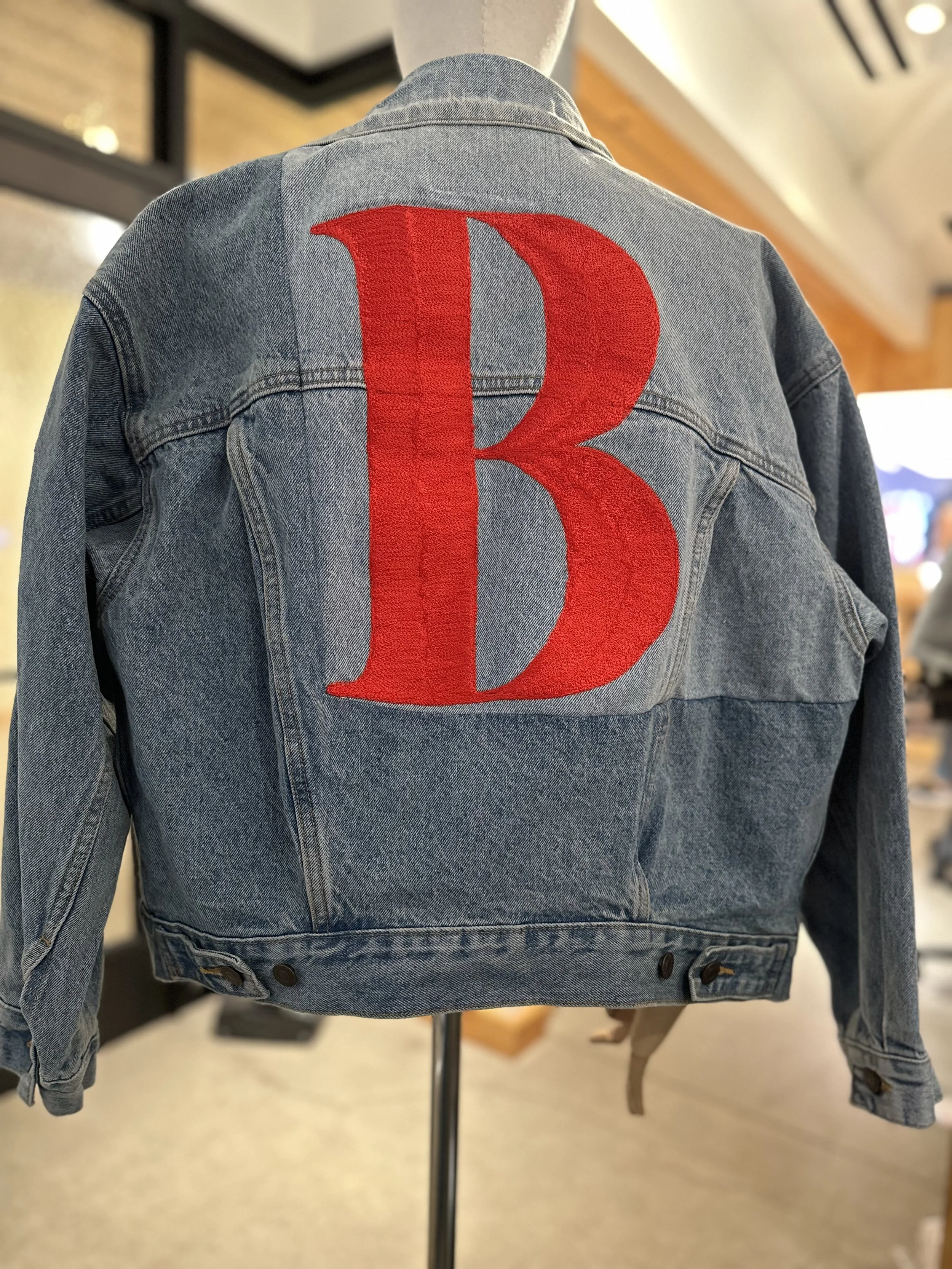 Back of a denim jacket with large red embroidered letter 'B' on the back.
