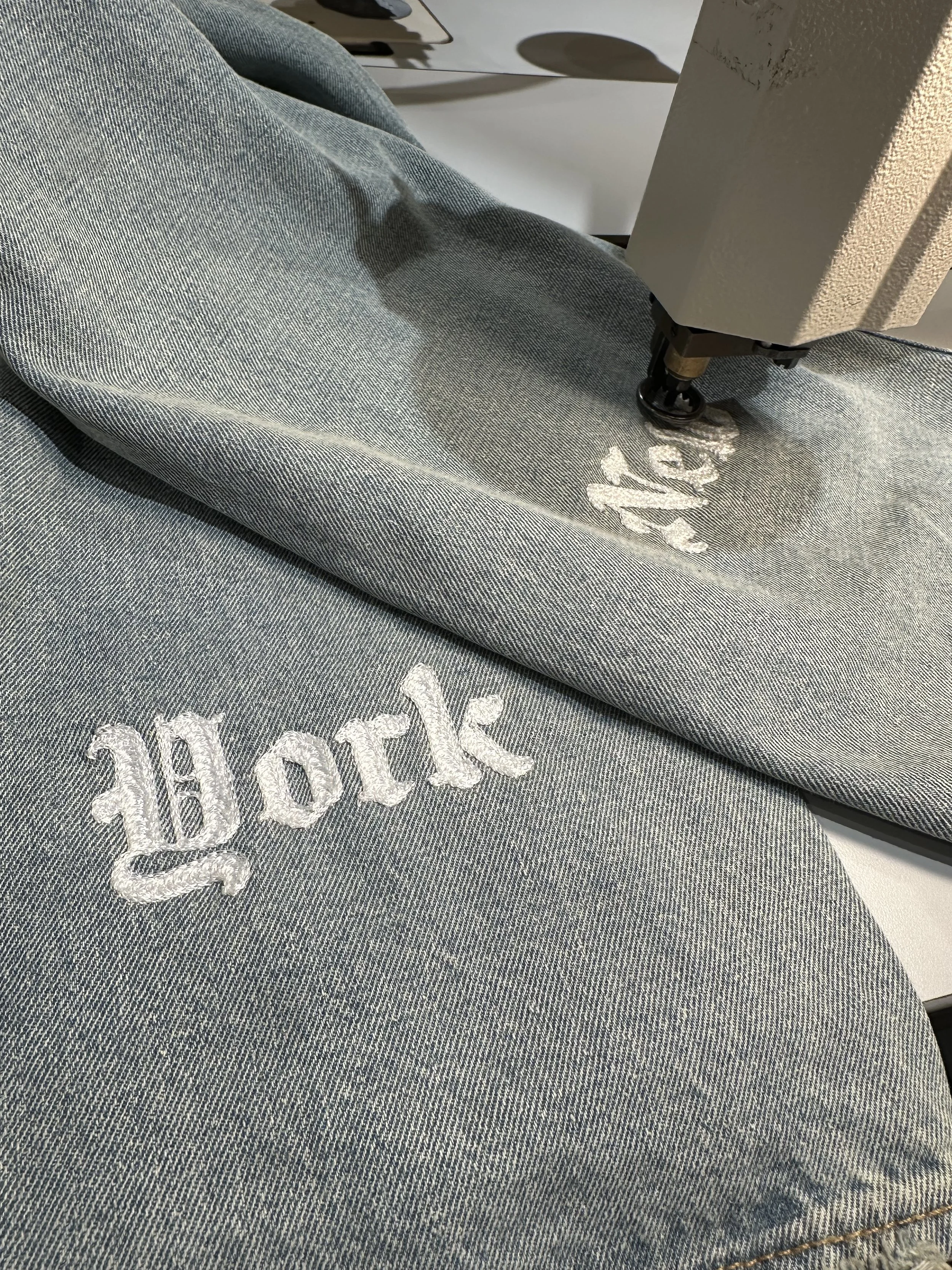 Close-up of a pair of blue jeans with white embroidered text reading 'hope' on the fabric.